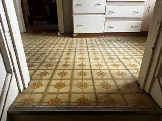 Vintage patterned sheet vinyl flooring in a kitchen entryway requiring a certified asbestos inspection prior to removal.