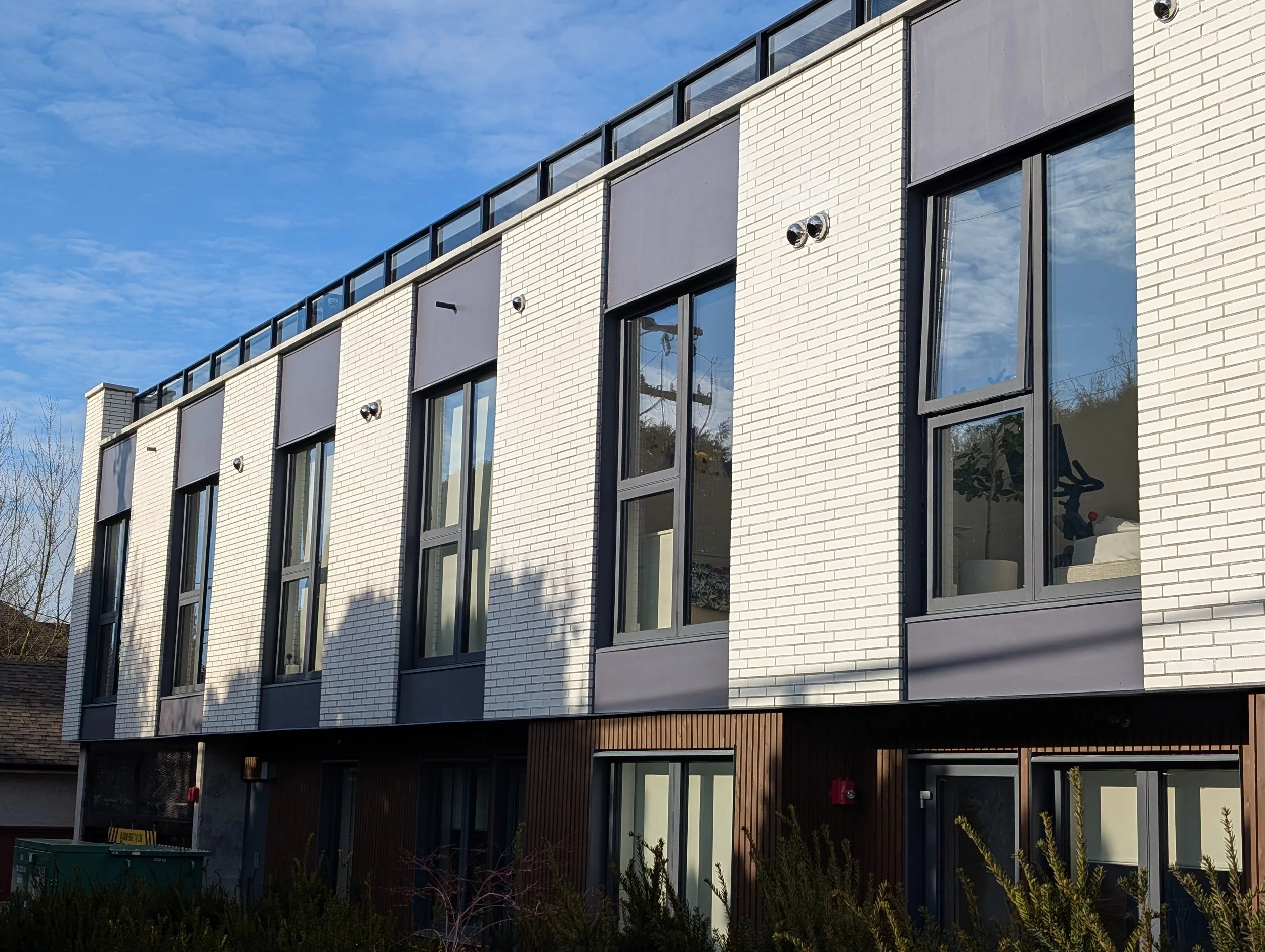 Modern building with white brick exterior, large windows, and rooftop railing, under a partly cloudy blue sky. Brick masonry design 
