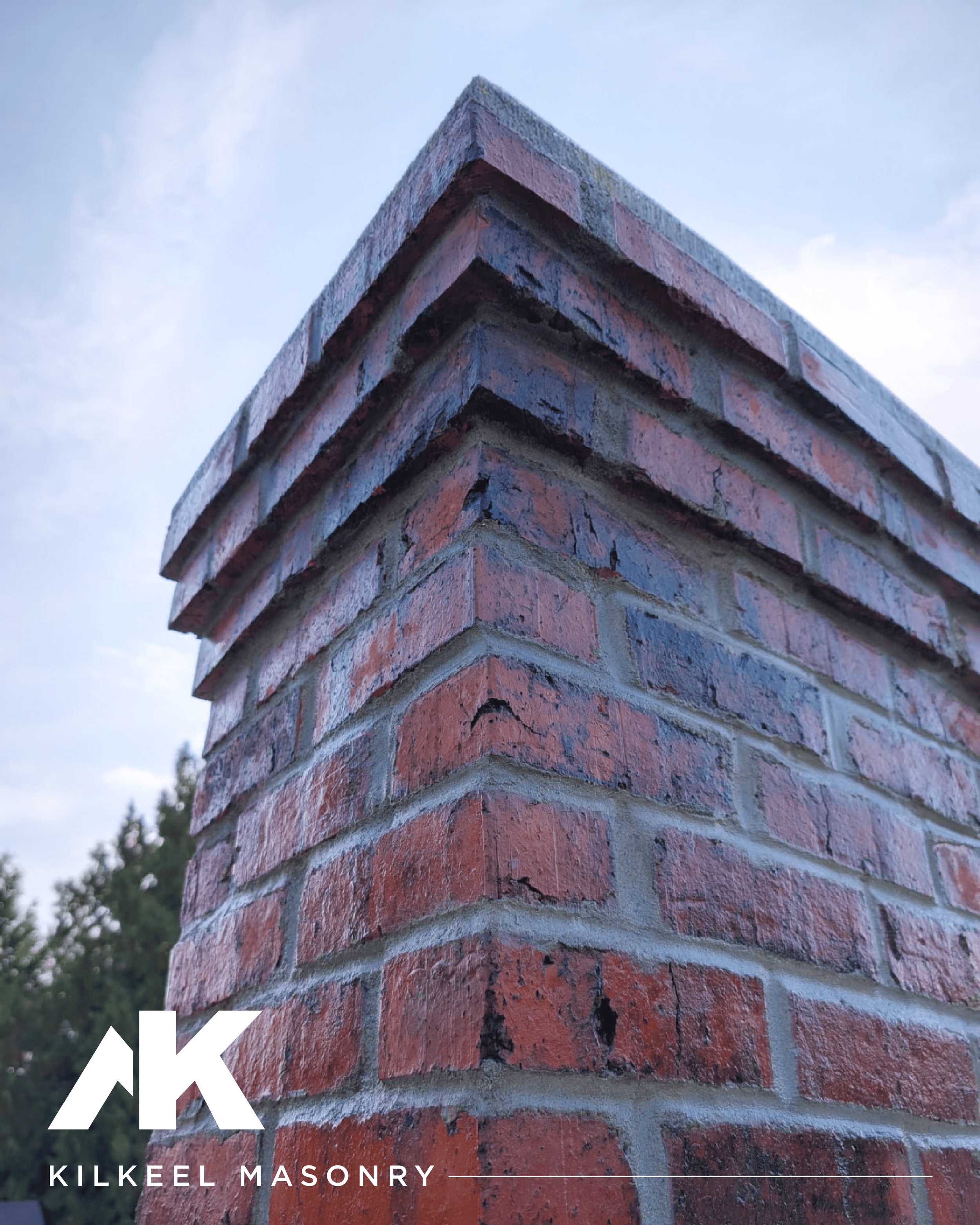 Close-up view of a brick corner of a building, with the sky and some trees in the background.