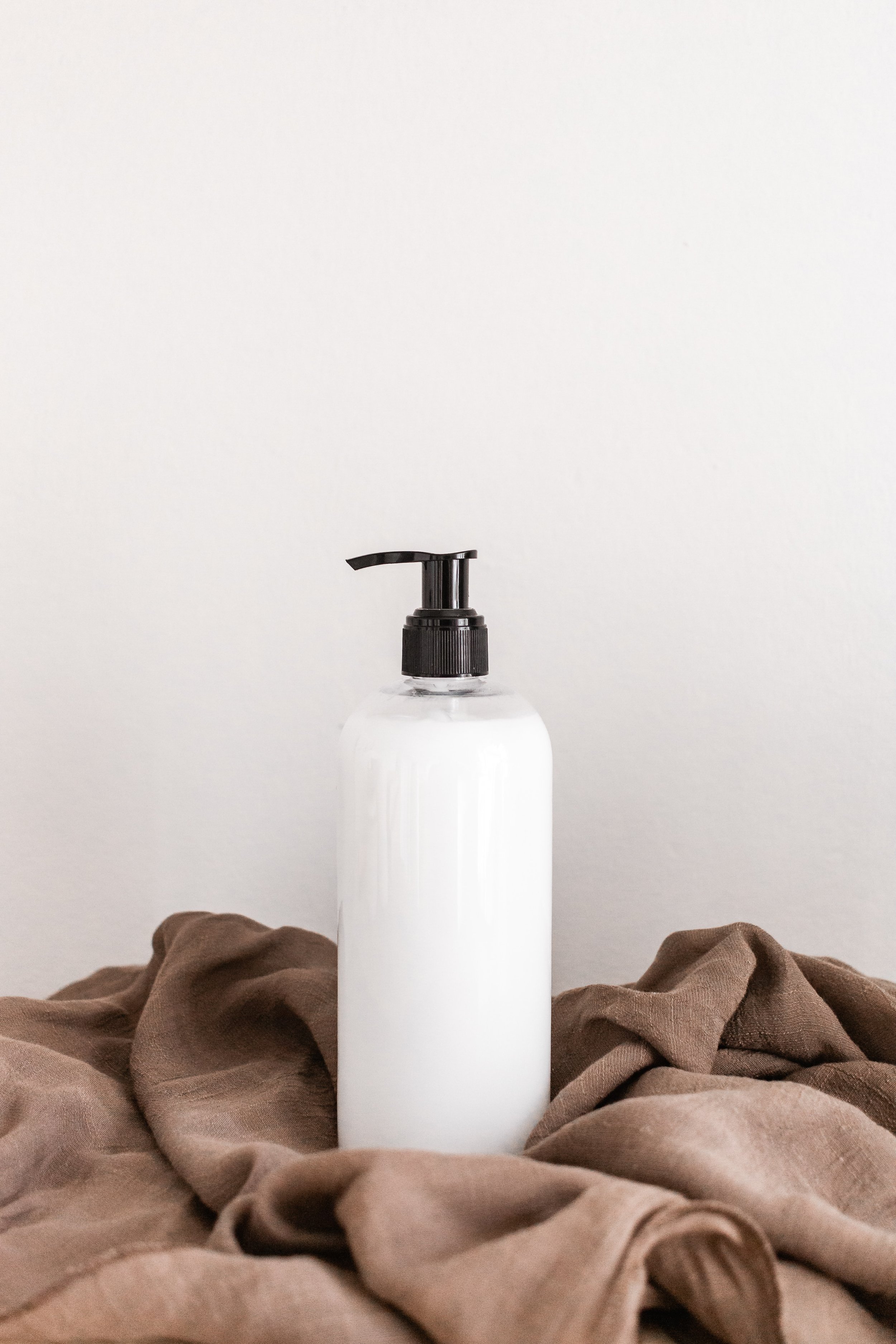 A white pump bottle on brown fabric against a plain white wall.