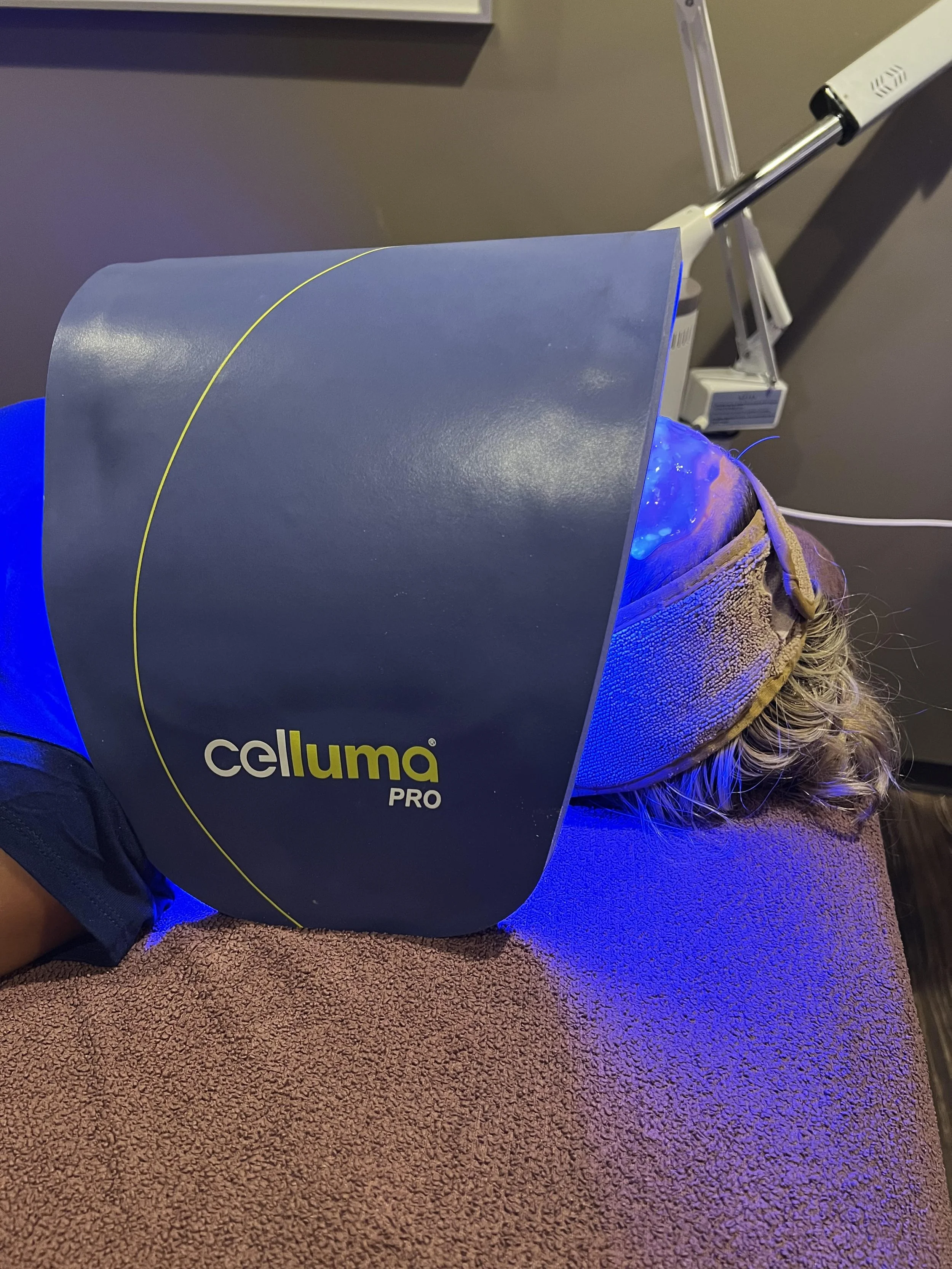A person receiving a skincare treatment with a Celluma Pro LED light therapy device, lying on a treatment table with a protective eye mask.