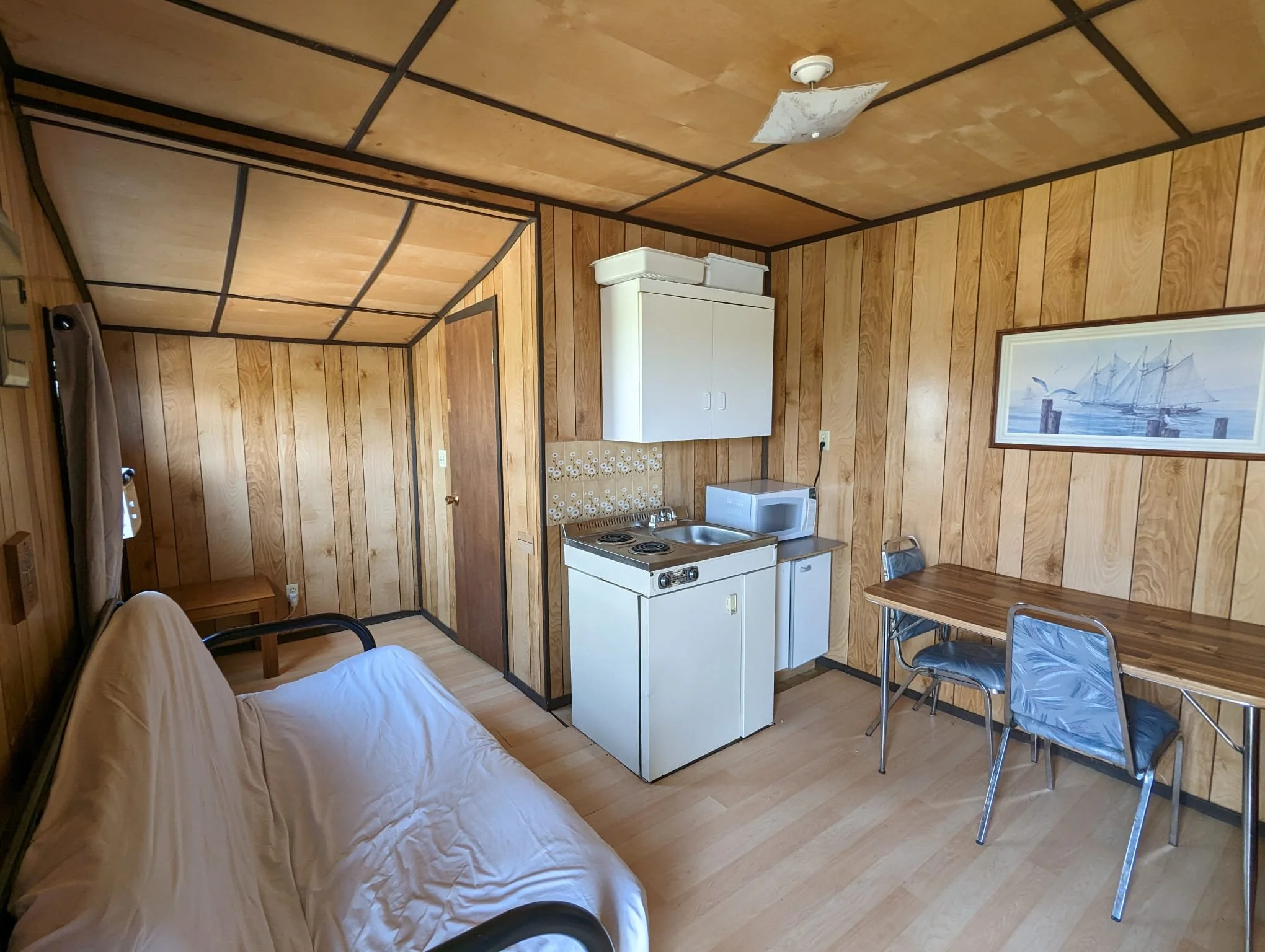 Kora Traditional Unit 6, Small wooden room with a futon, kitchenette area with a mini fridge, microwave, and stovetop, a small dining table with chairs