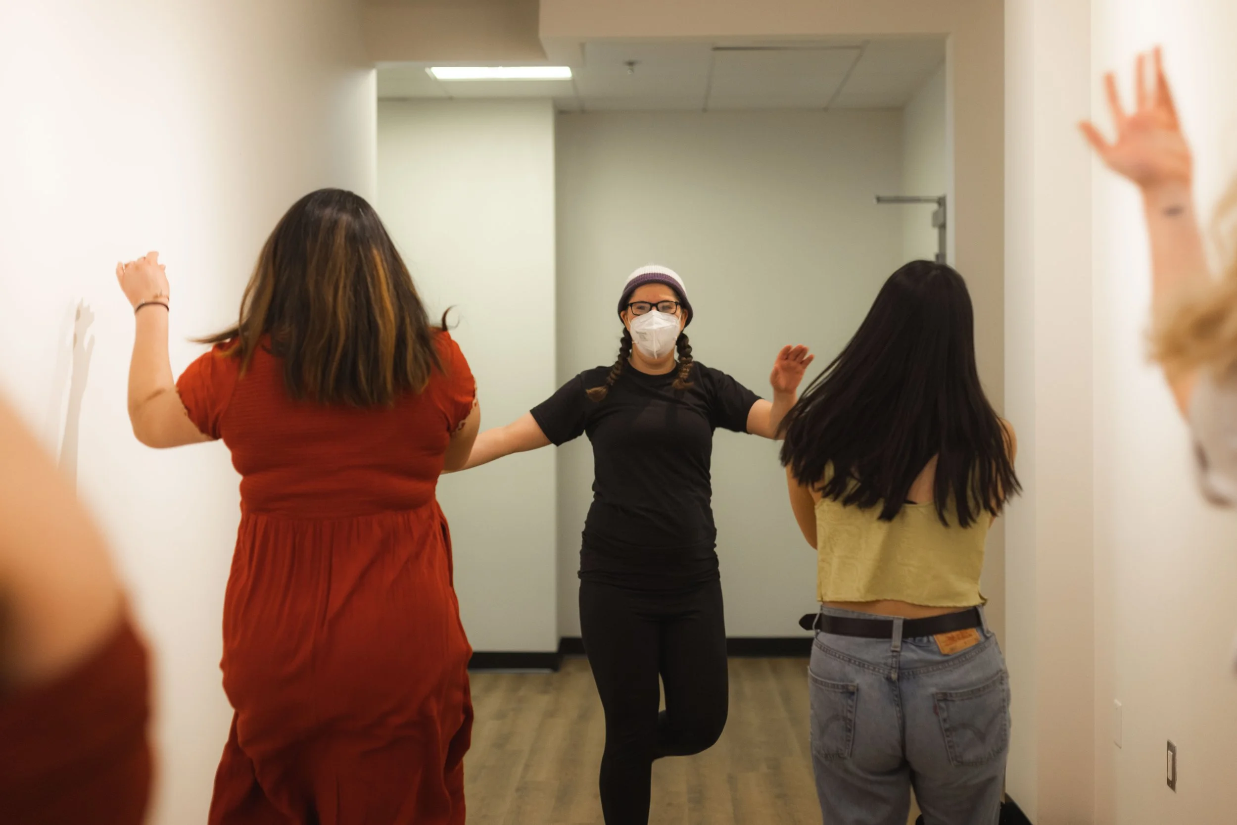 A white, masked nonbinary person raises their arms and leads two other students in happy dancing.