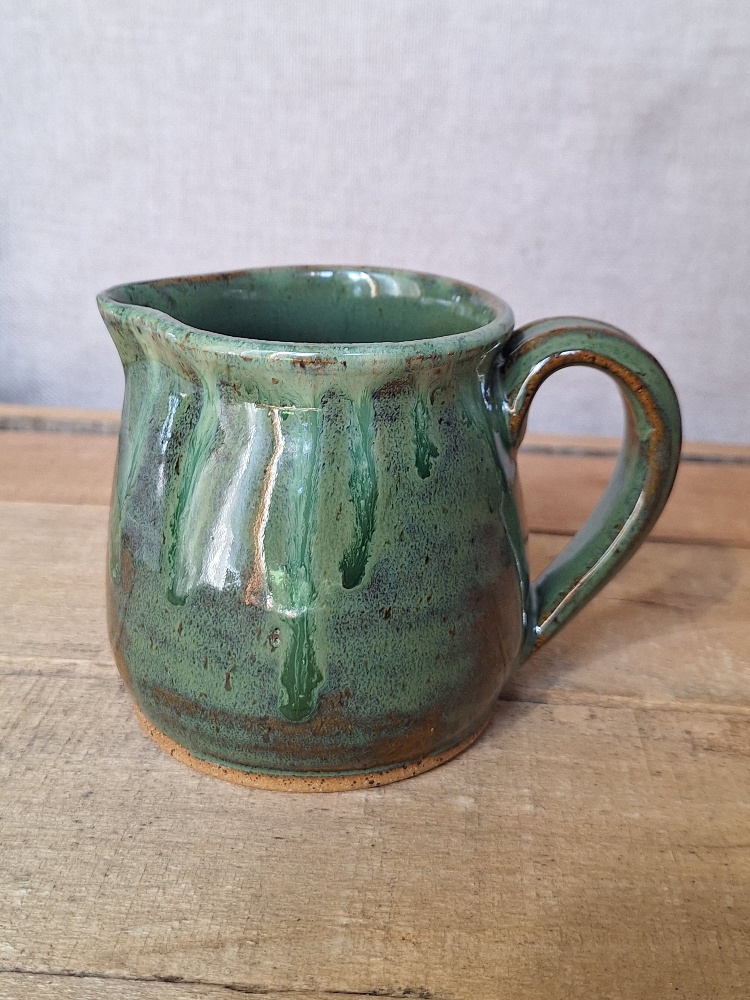 Green ceramic mug with a glossy glaze and drip pattern, sitting on a wooden surface.