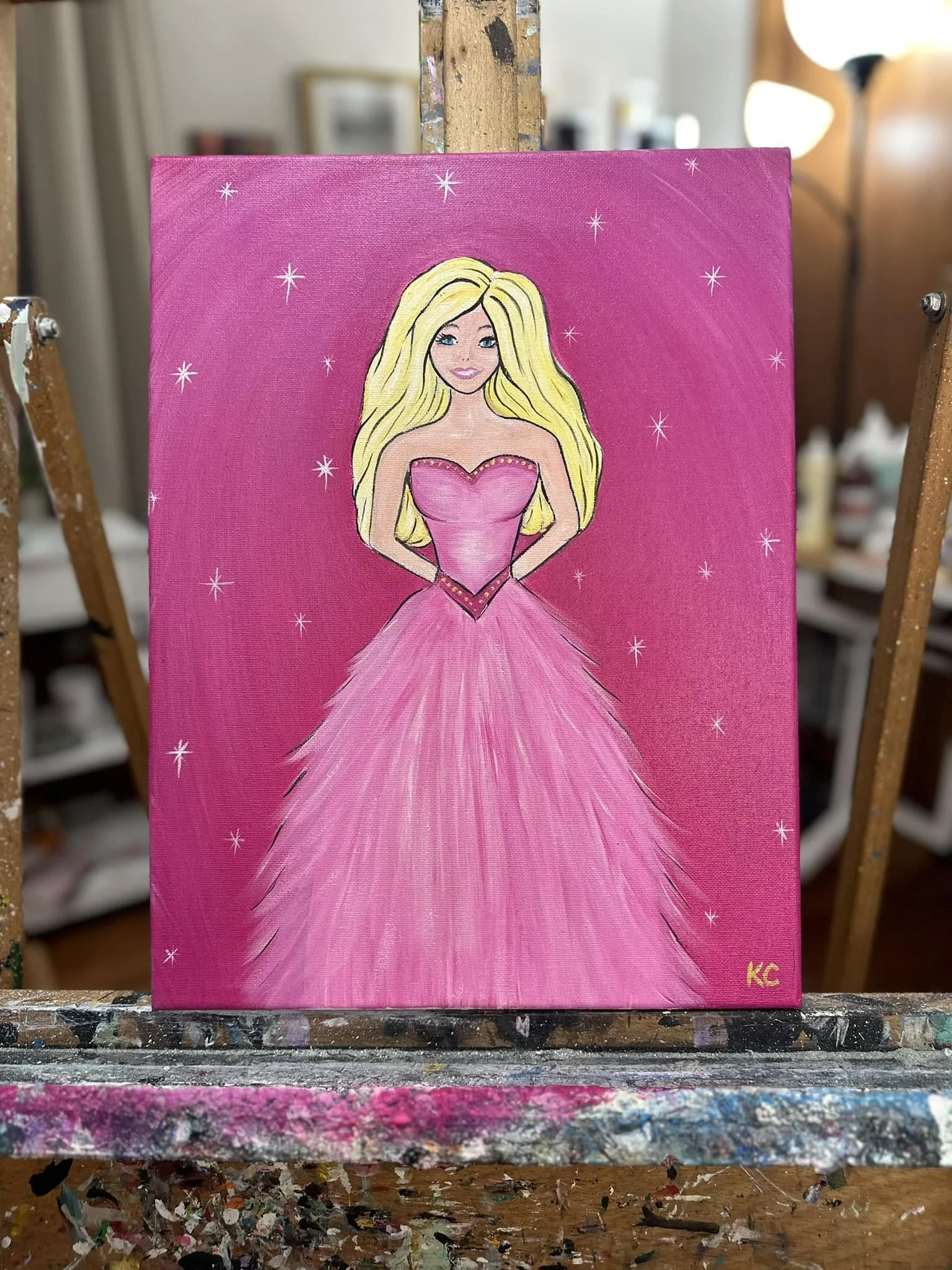 Painting of a blonde woman in a pink gown with a fitted bodice and a full, layered skirt, standing against a pink background with small white stars. The painting is signed 'KC' in yellow at the bottom right corner.