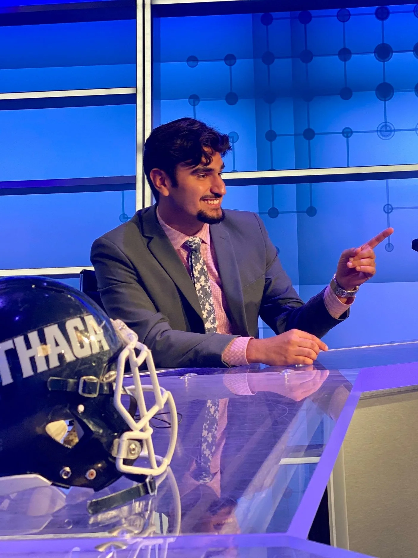 Jayden Becker serving as a studio host at the anchor desk during a sports broadcast.