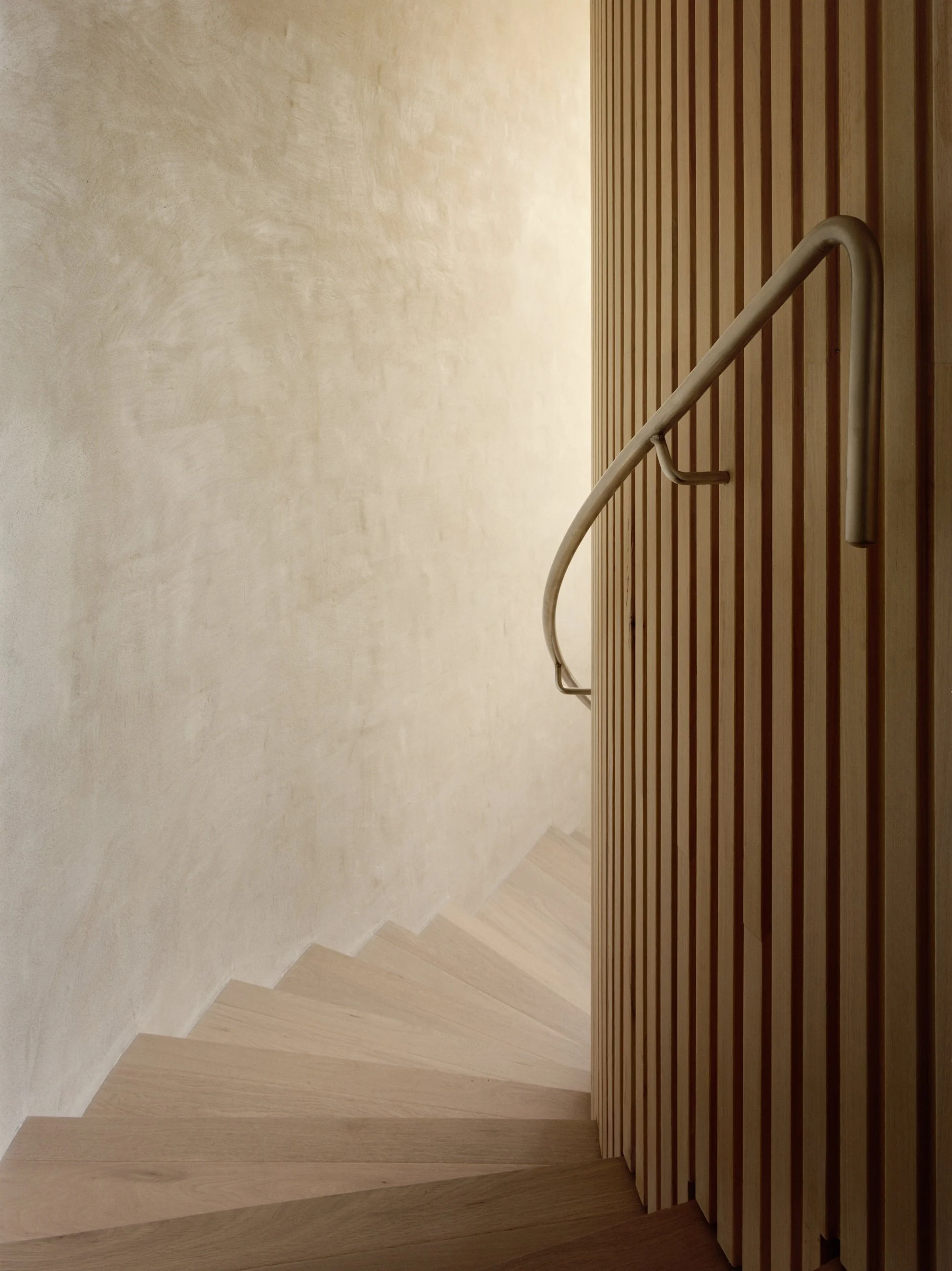 Wooden staircase with metal handrail next to a wooden slat wall and beige textured wall.