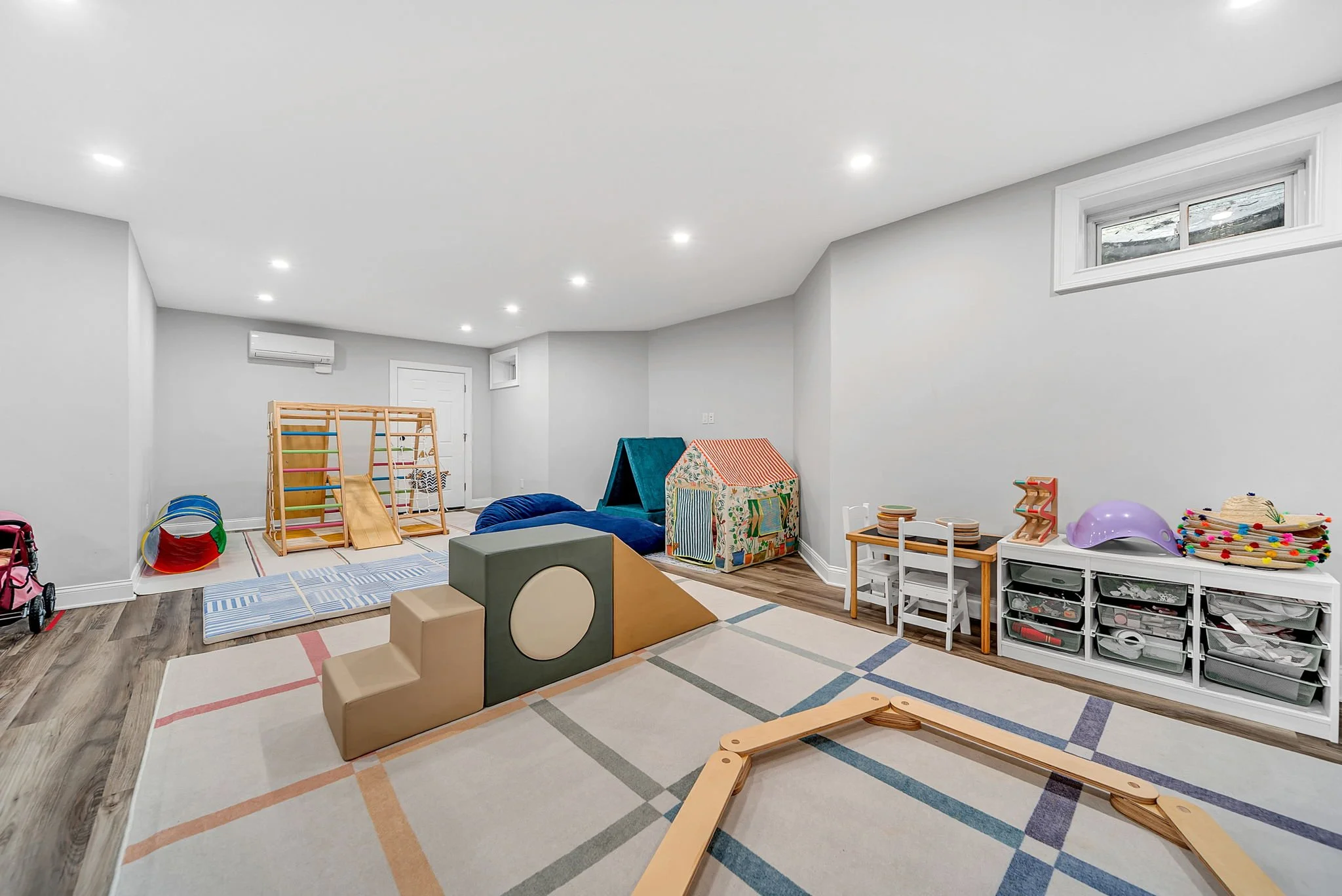 Children's playroom with toys, climbing structures, small table and chairs, storage bins, and colorful decorations.