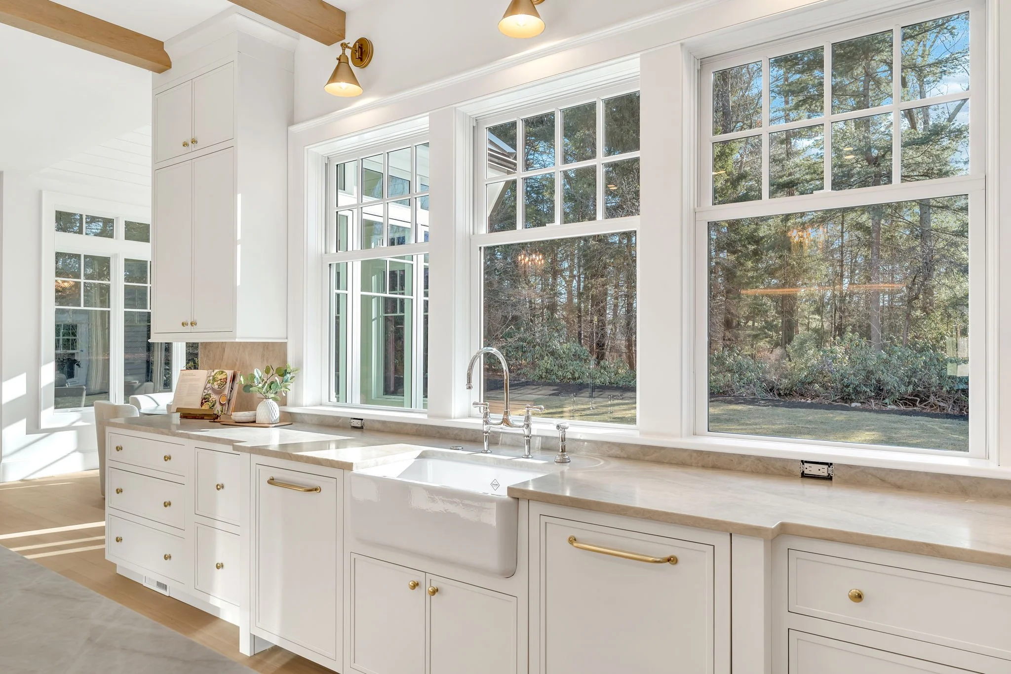 Bright kitchen with white cabinets, beige countertop, large windows, and a view of trees outside.