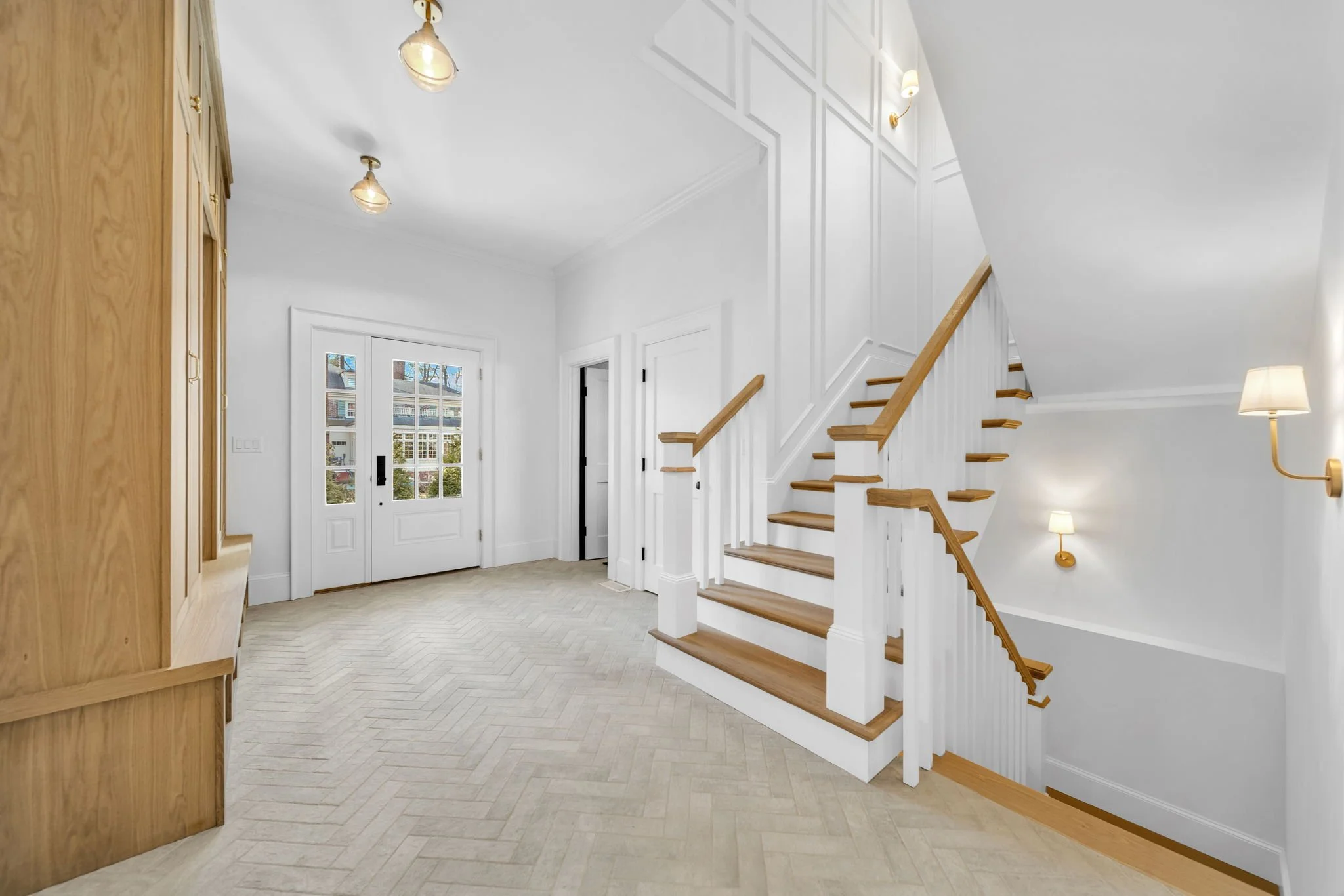 Bright entryway with white walls, wooden staircase, and multiple light fixtures.