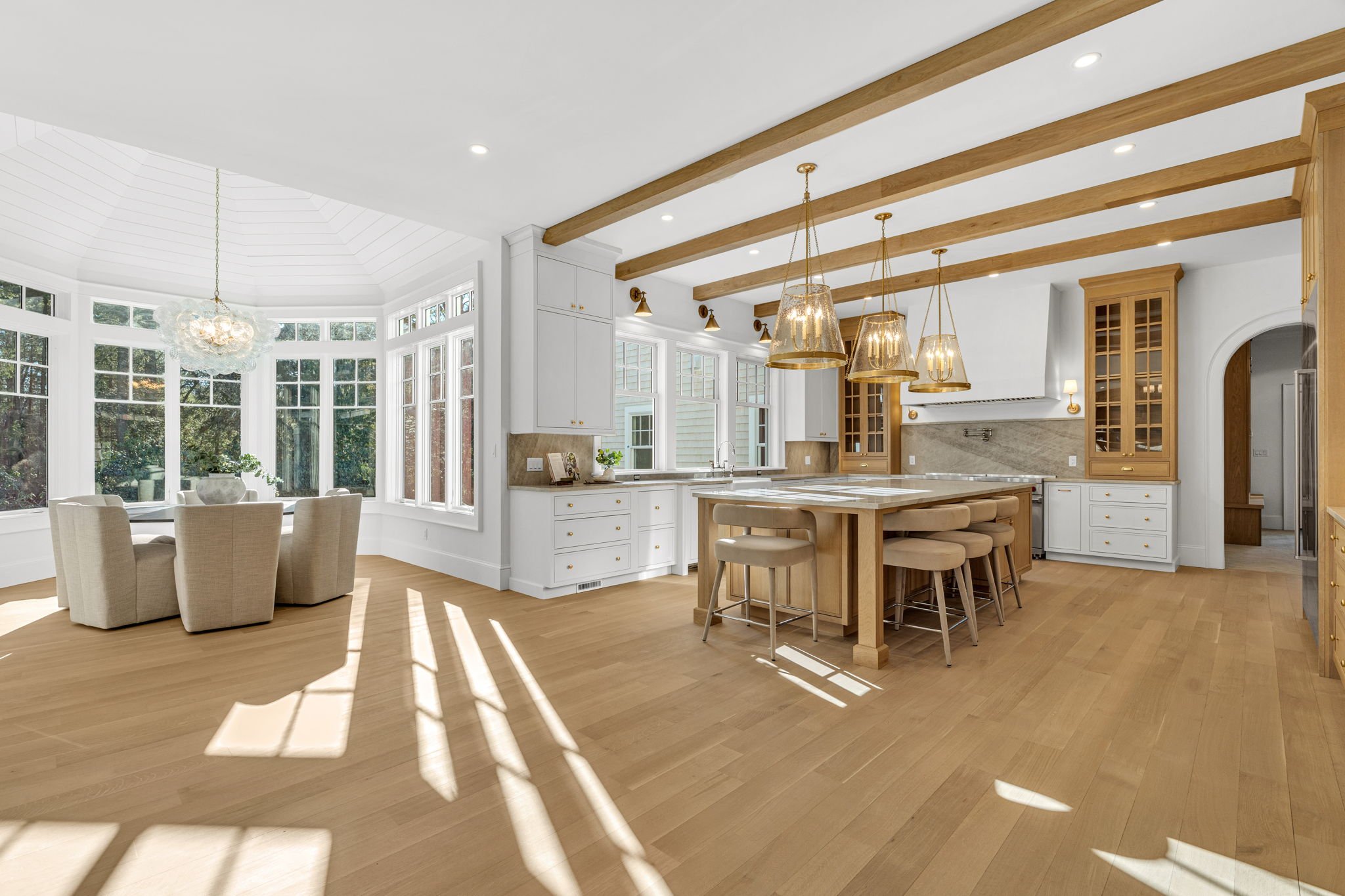 Bright open kitchen and dining area with hardwood floors, white cabinets, a kitchen island, pendant lights, and large windows