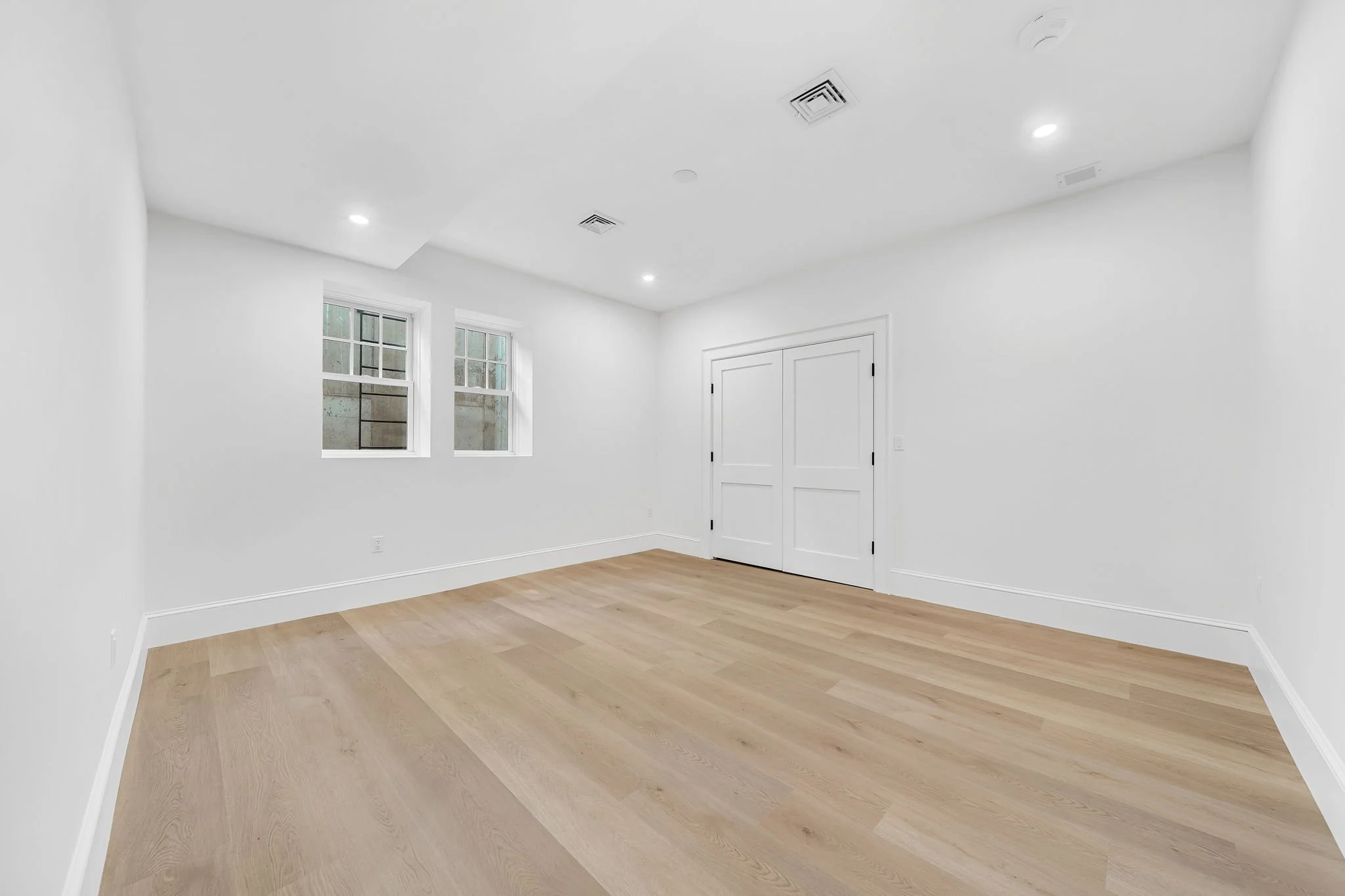 Empty room with white walls, hardwood floor, two windows, and a closed door.