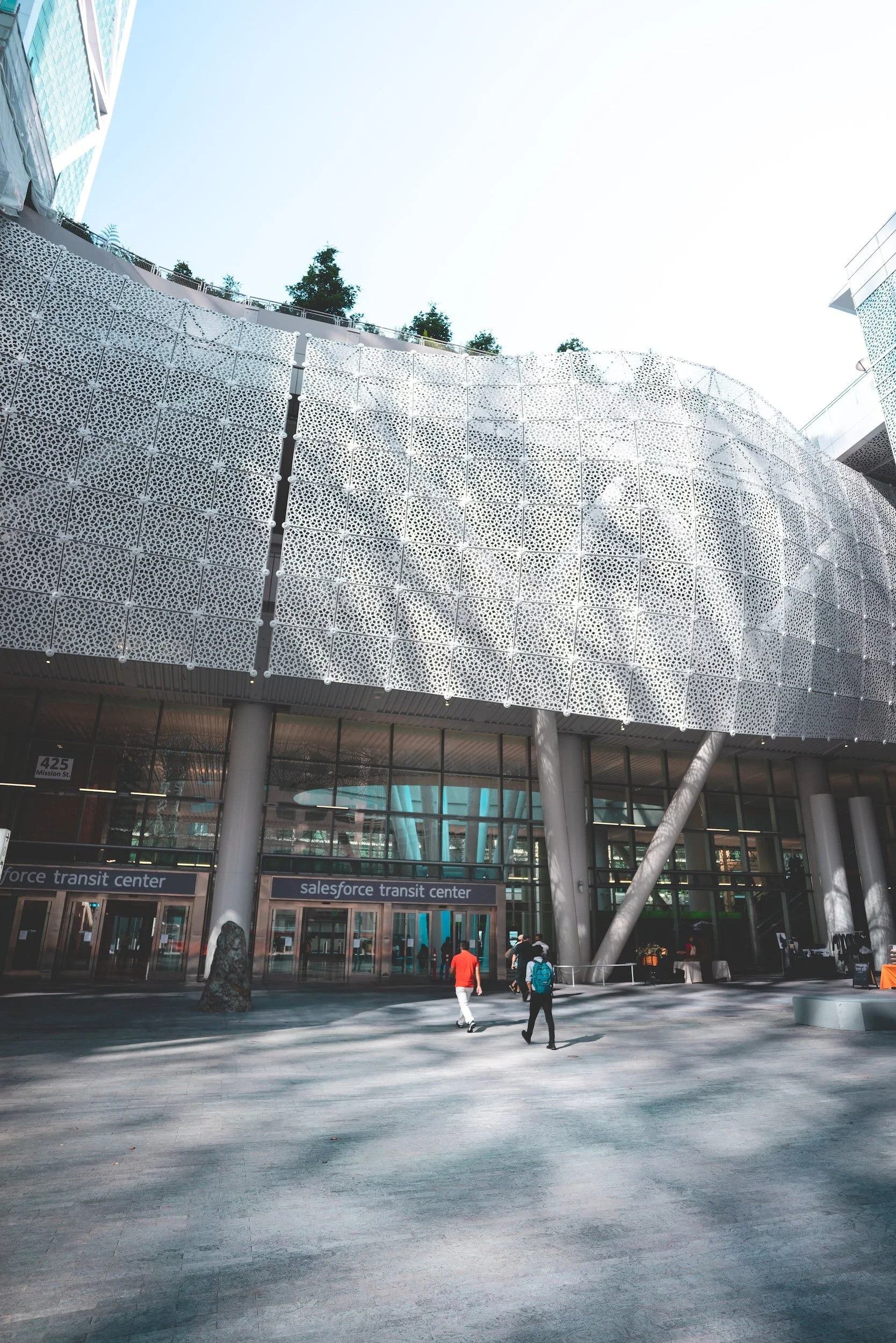 People walking outside the Salesforce Transit Center with a modern architectural facade and metallic panels.