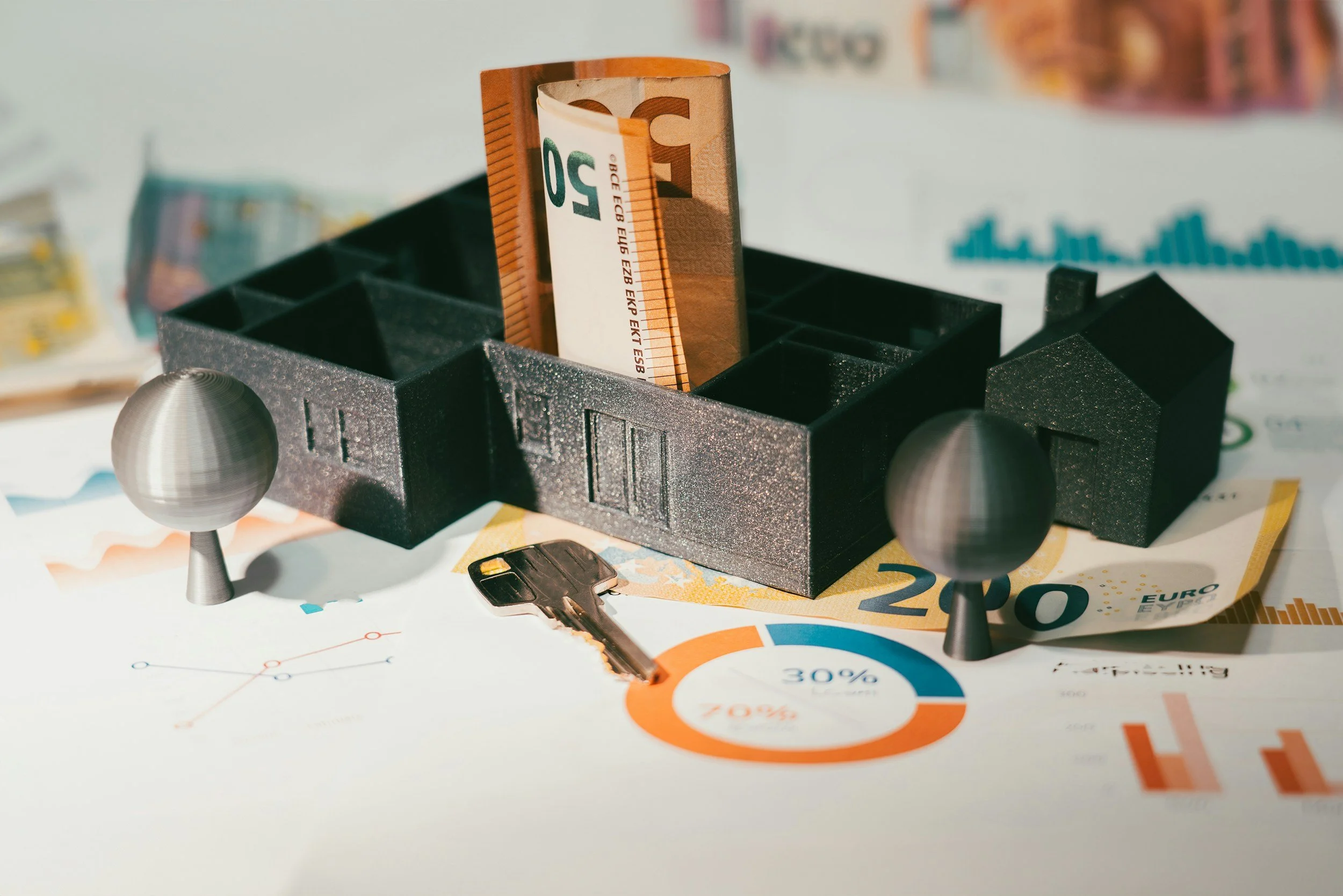 Euro bills placed in a black, textured cardholder with black spherical handles, surrounded by scattered paper documents and a small black key.