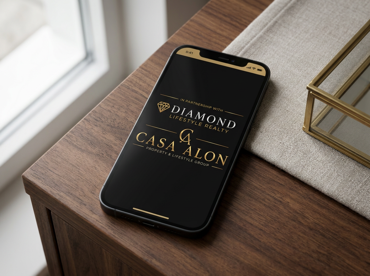 Smartphone on wooden table displaying logos for Diamond Lifestyle Realty and Casa Alon Property & Lifestyle Group in gold and white on a black background.