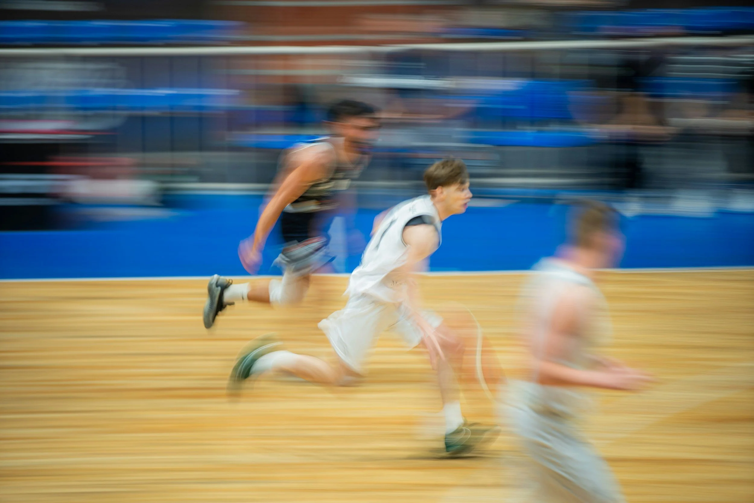 Blurred action shot of young boys running on an indoor basketball court during a game.
