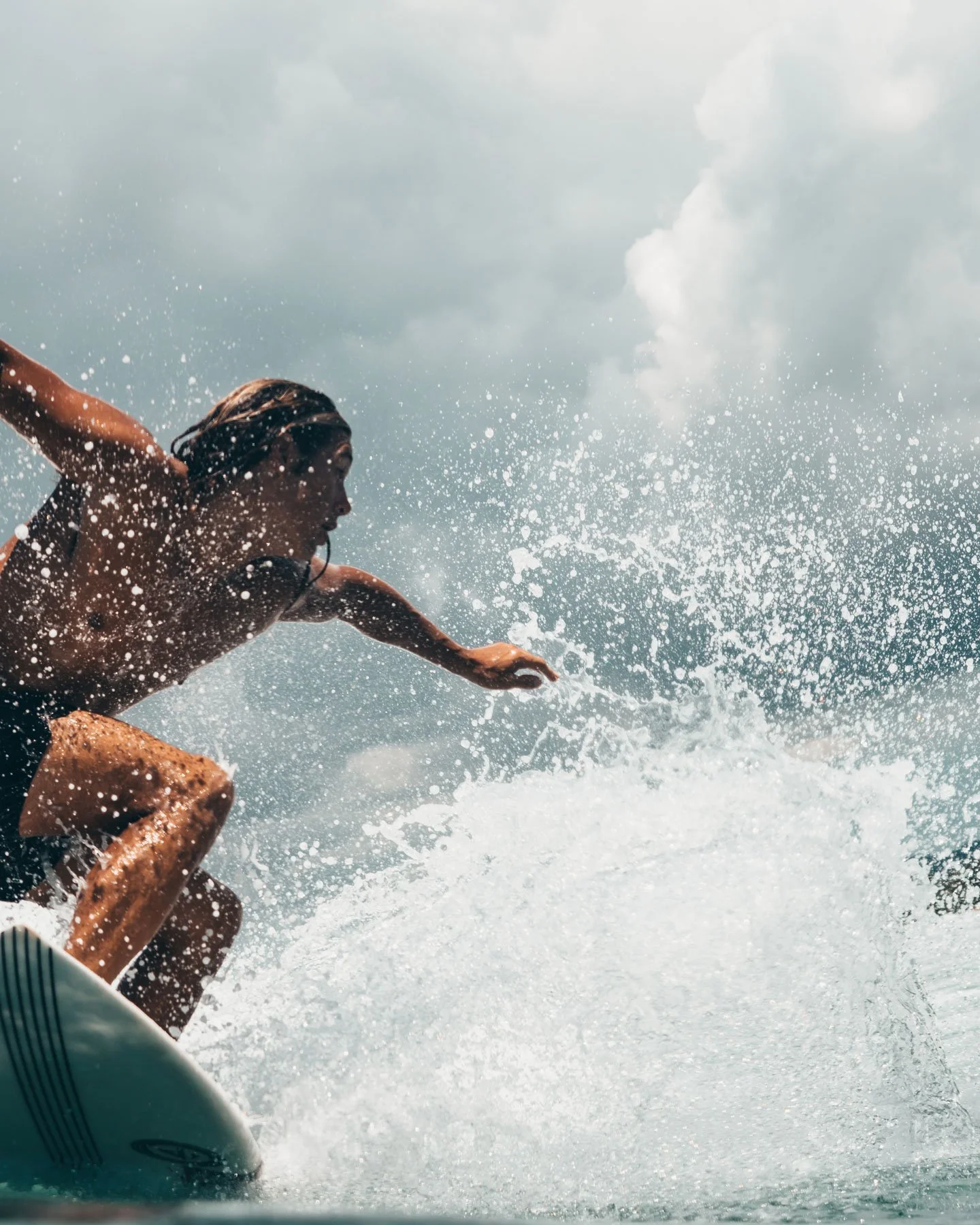 A young person with long hair surfing a wave in the ocean during daytime