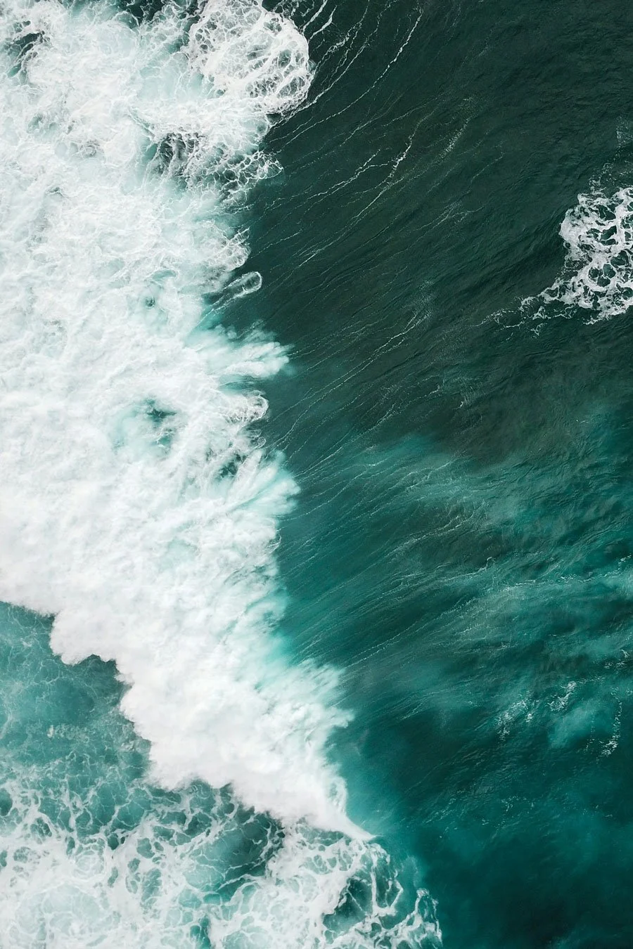 Aerial view of ocean waves crashing and creating white foam and spray.