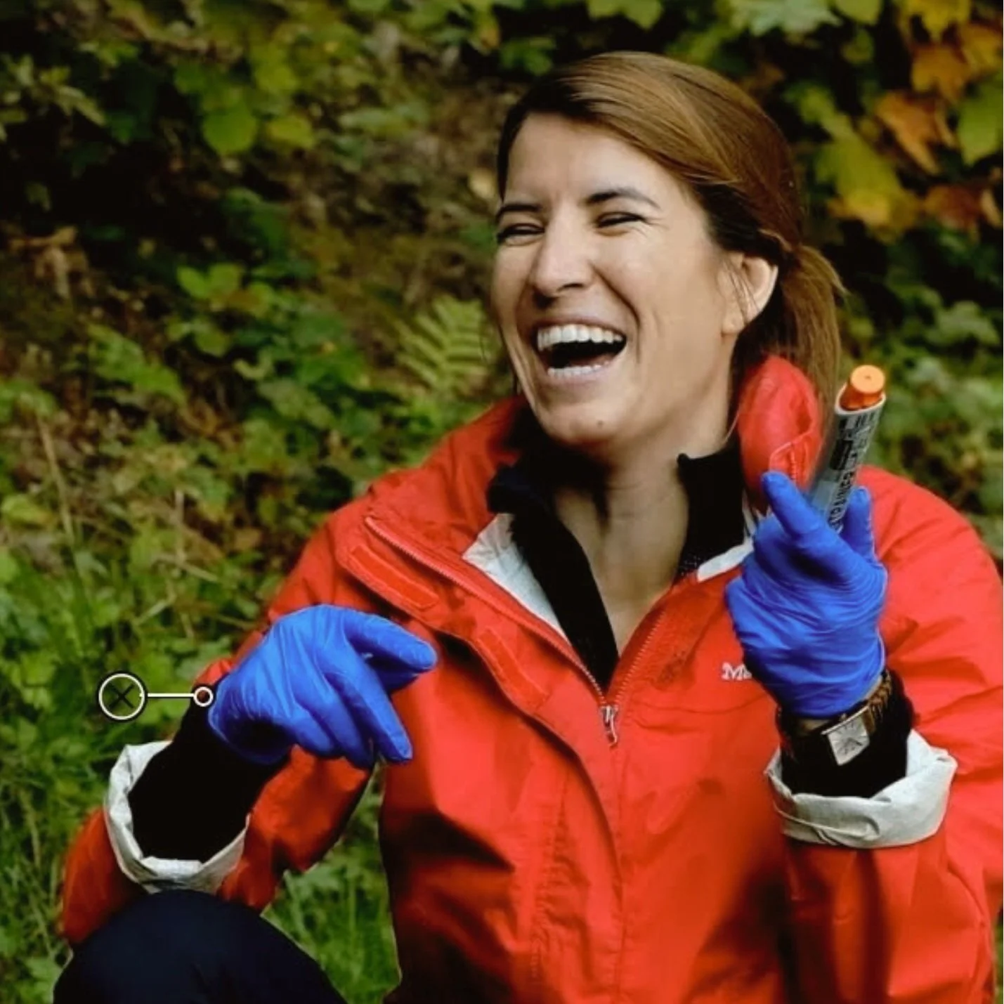 Person outdoors wearing a red jacket and blue gloves, laughing and holding an object.