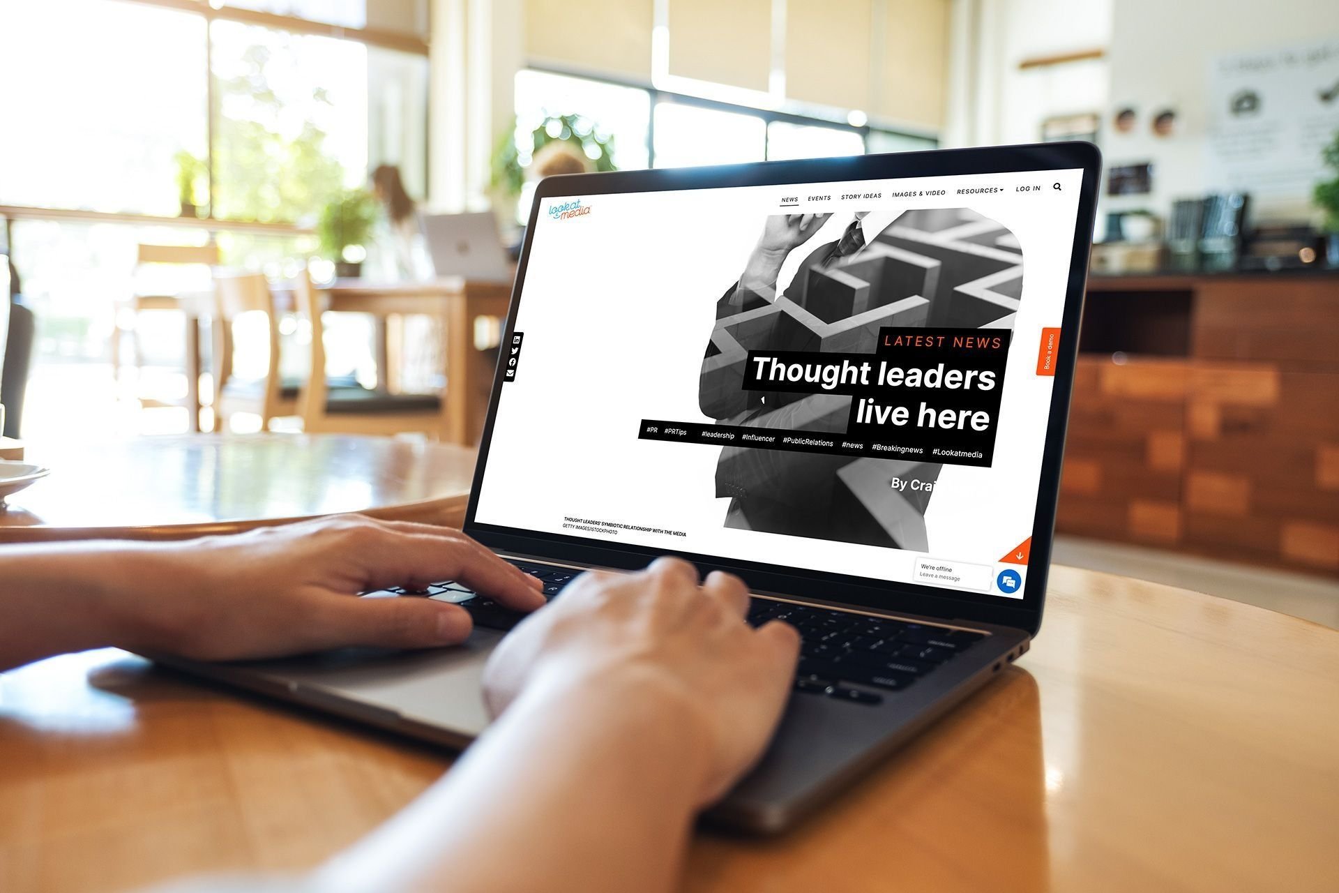 Person working on a laptop in a well-lit coffee shop or office, viewing a webpage with the headline 'Thought leaders live here' and a black-and-white graphic of a person in a suit.