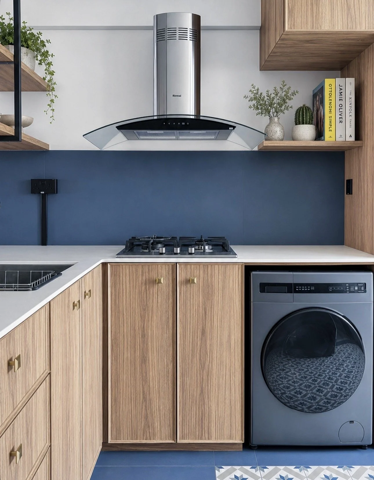 Modern kitchen with wooden cabinets, a gas stove, a range hood, and a washing machine, decorated with potted plants and books.