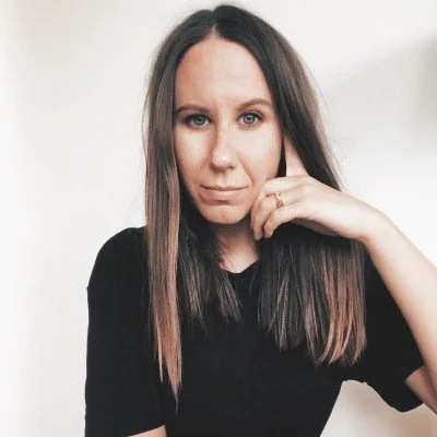 Woman with long hair wearing a black shirt, posing thoughtfully against a white background.
