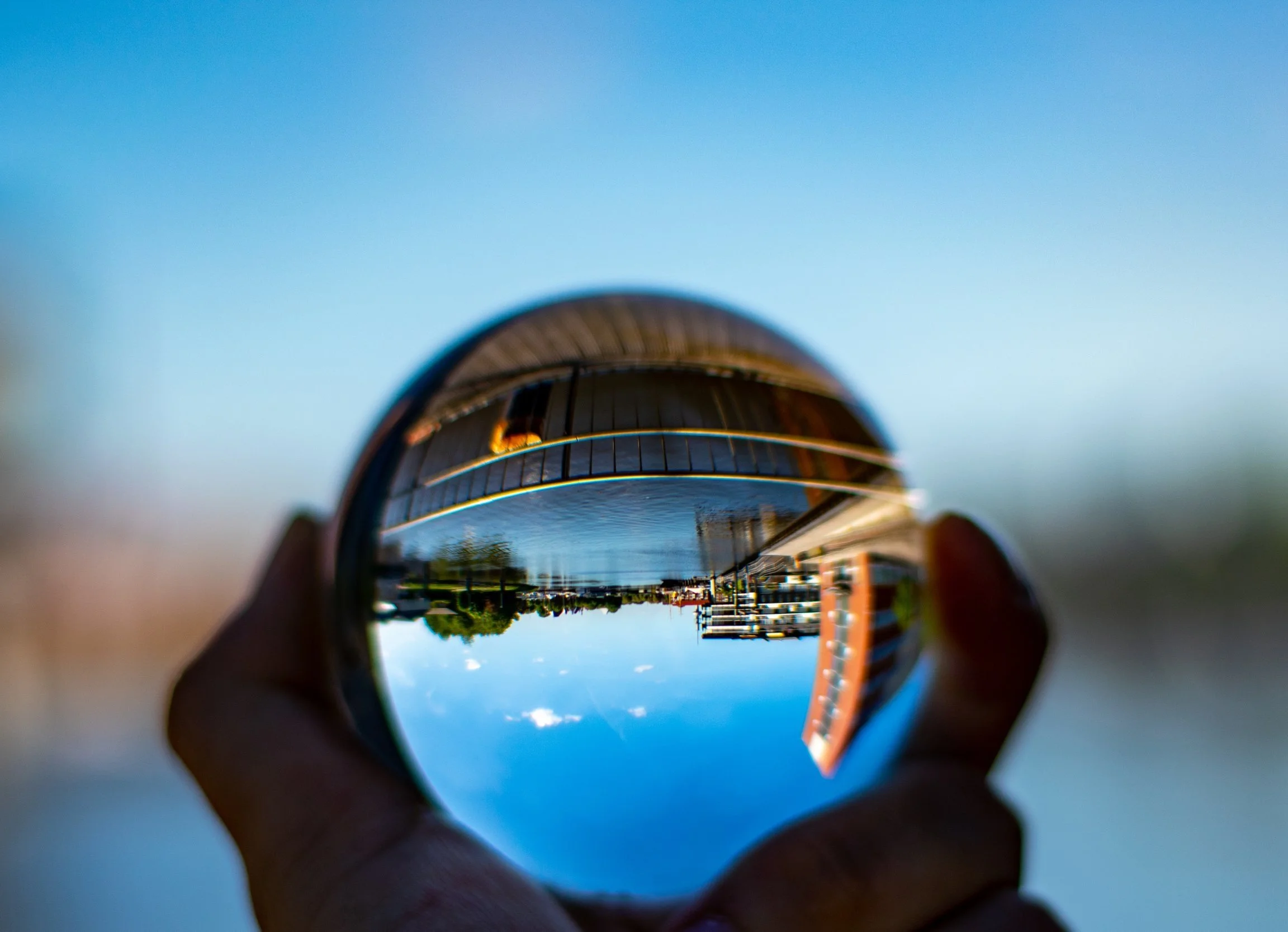Vaso de cristal con vista de una calle y edificios reflejada, en un día soleado.
