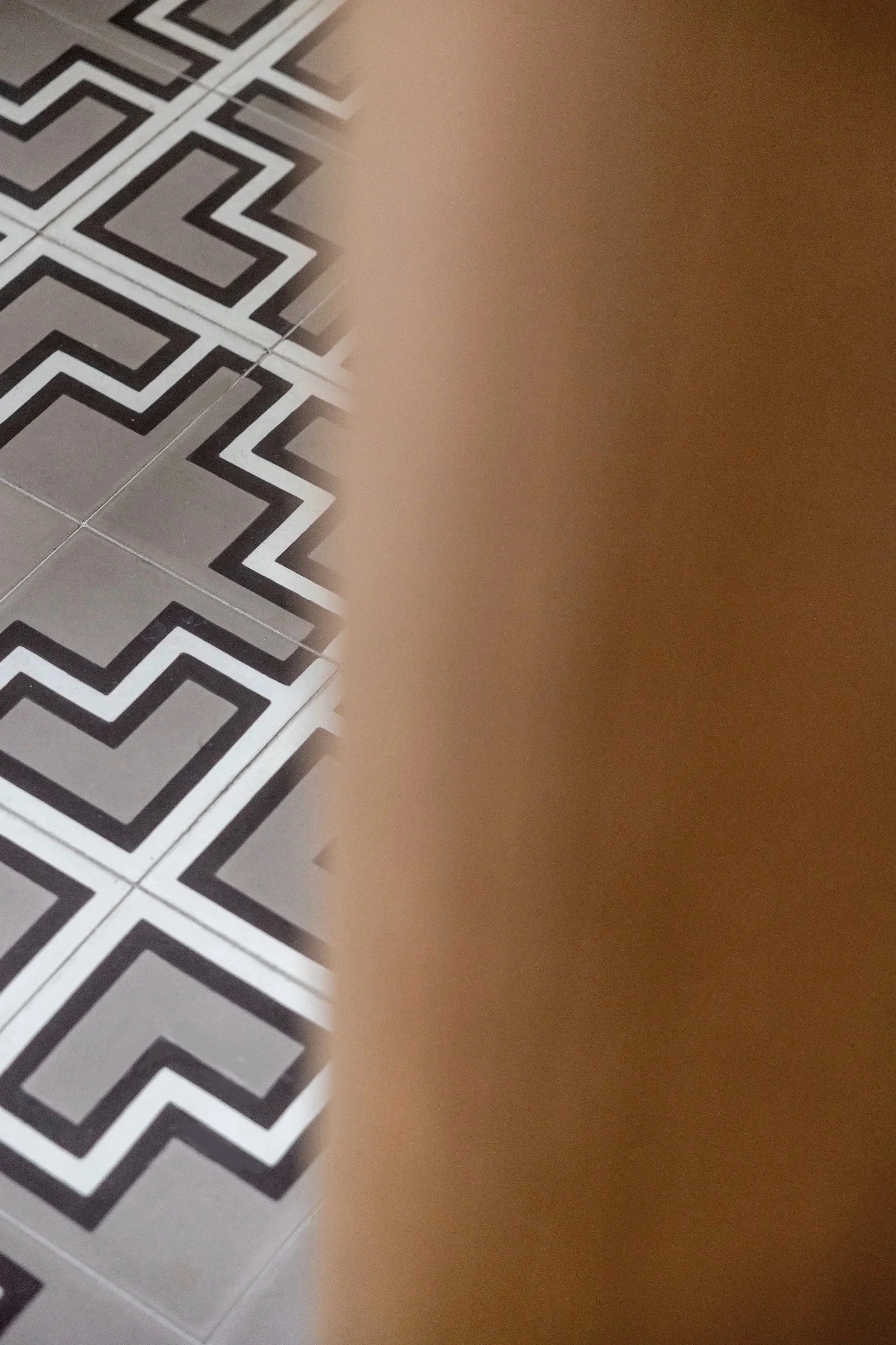 Carrelage de sol avec un motif géométrique noir, blanc et gris, partiellement caché par des agencements sur mesure en chêne clair.