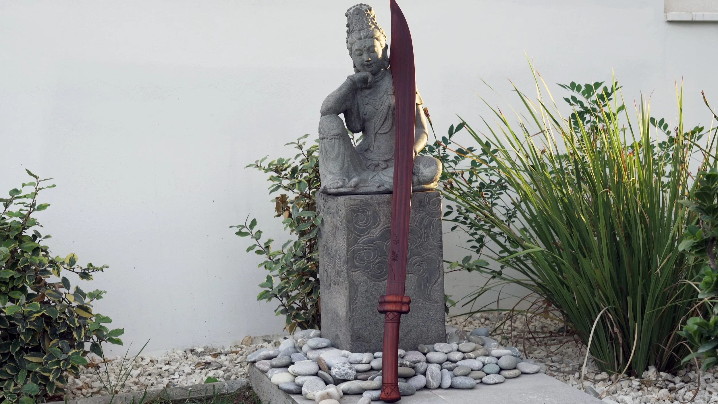Red sandalwood wooden Dao broadsword standing against a carved stone statue