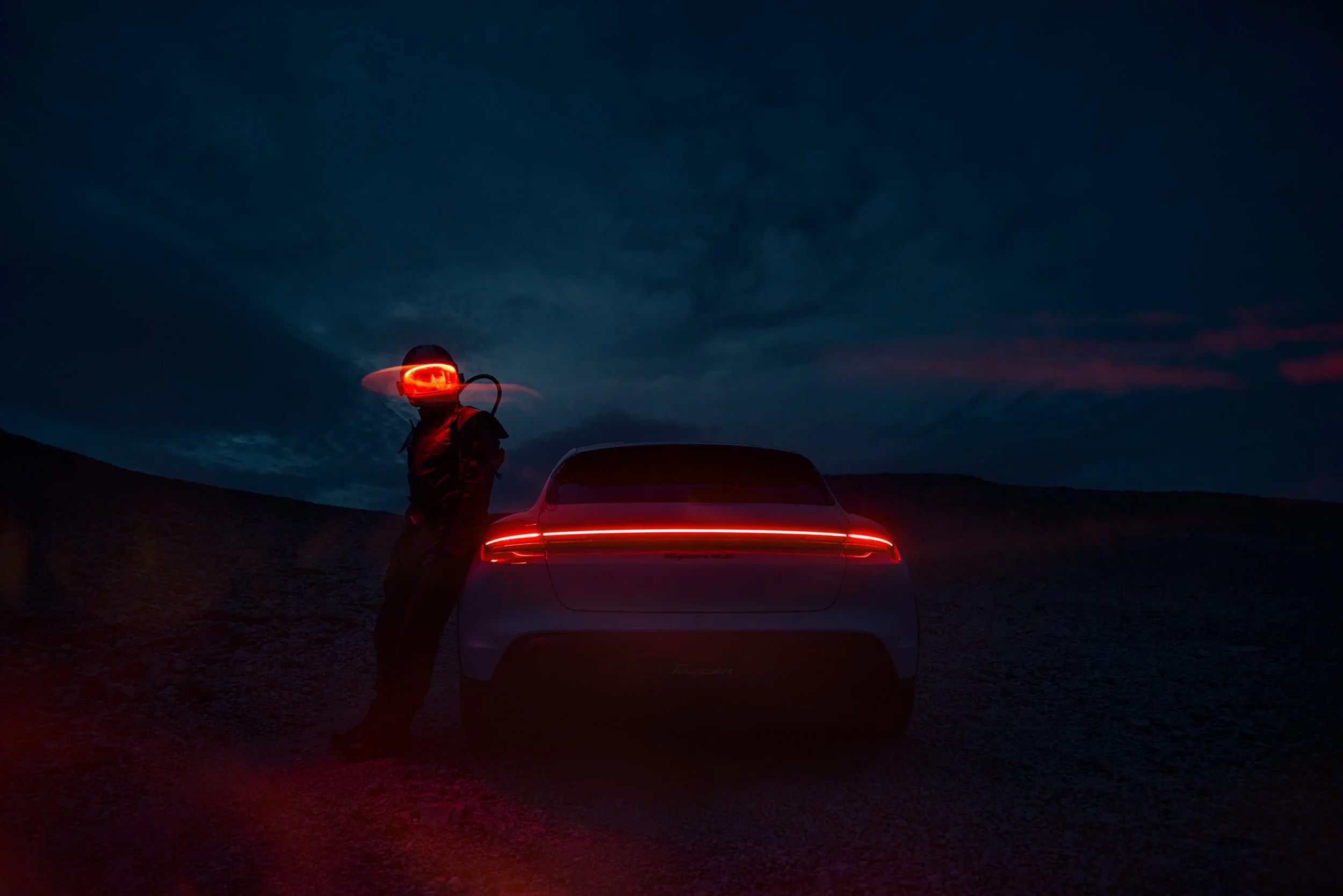 High-end automotive image of a white electric SUV on rocky desert terrain at night with an Explorer, showcasing cinematic lighting and professional retouching.
