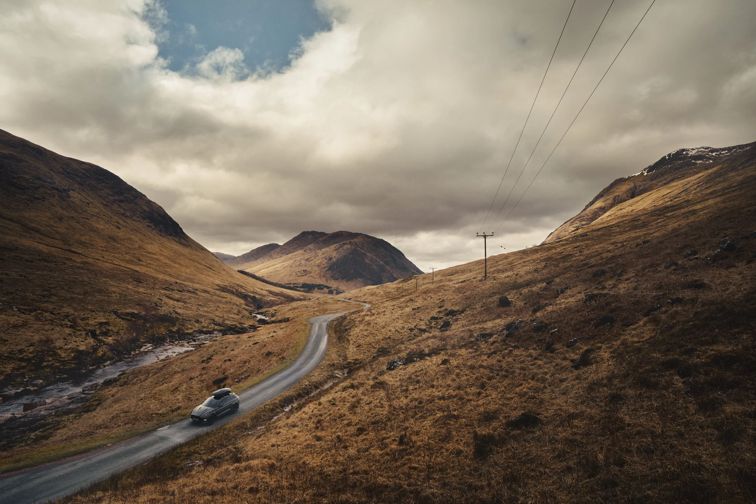 Photoreal automotive CGI scene of a luxury SUV in a rugged mountain landscape with cinematic lighting, demonstrating high-end compositing, retouching, and post-production for automotive advertising.