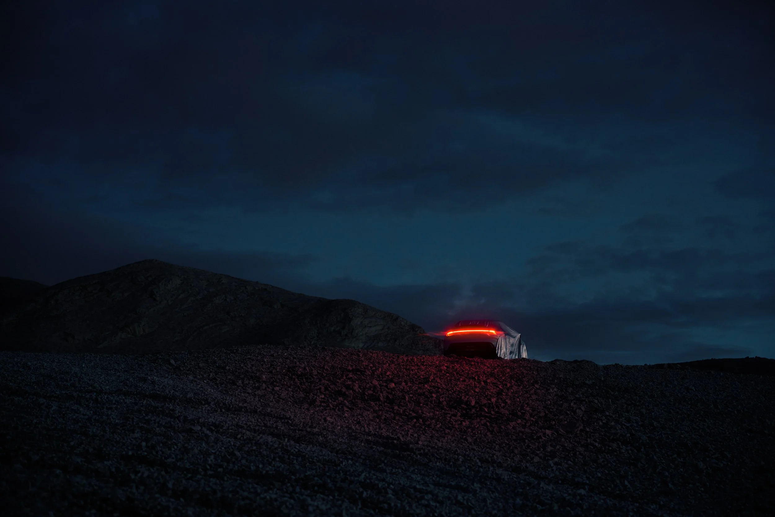 High-end automotive image of a white electric SUV on rocky desert terrain in the night, showcasing cinematic lighting and professional retouching.
