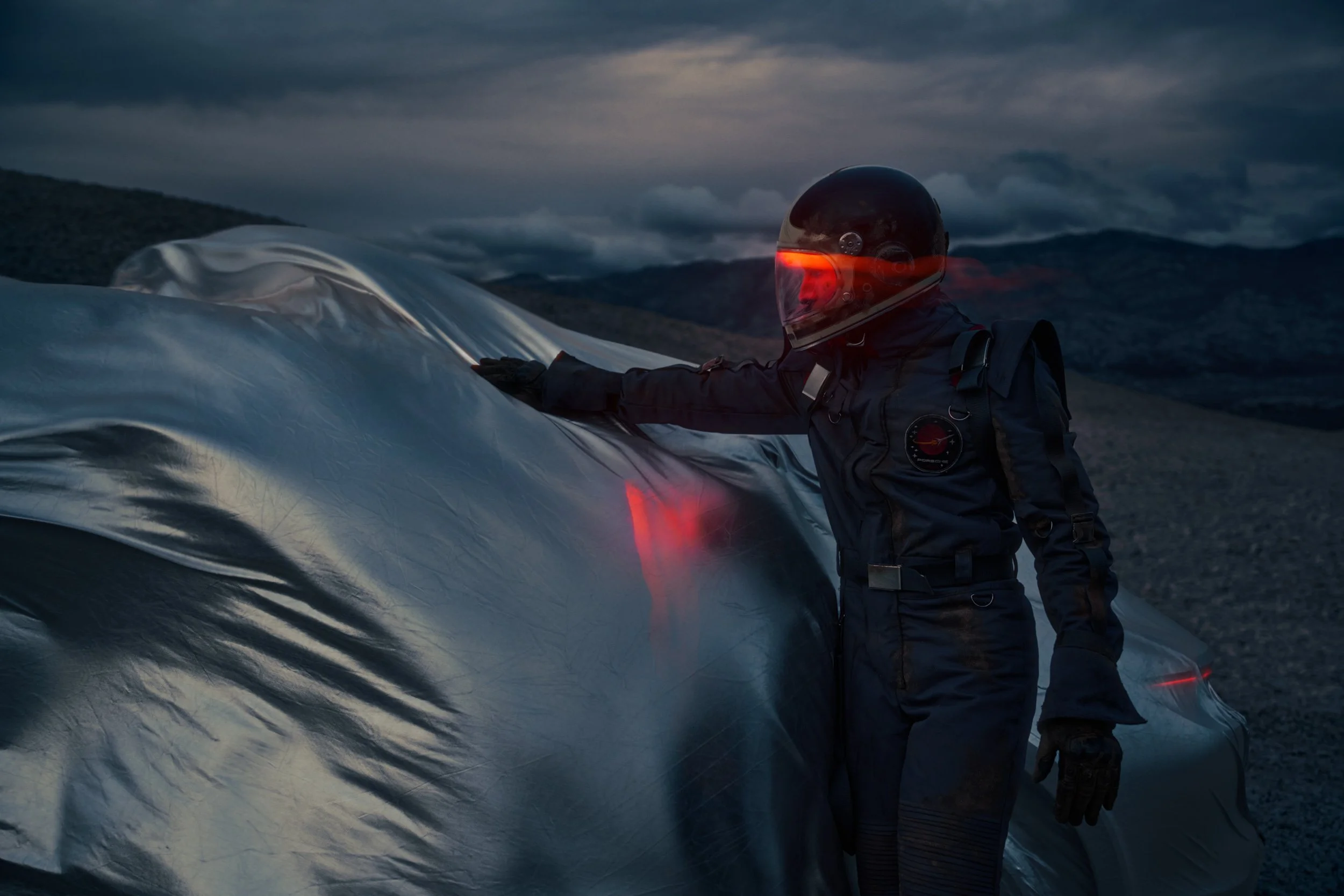 High-end automotive image of a white electric SUV on rocky desert terrain at dusk with an explorer, showcasing cinematic lighting and professional retouching.
