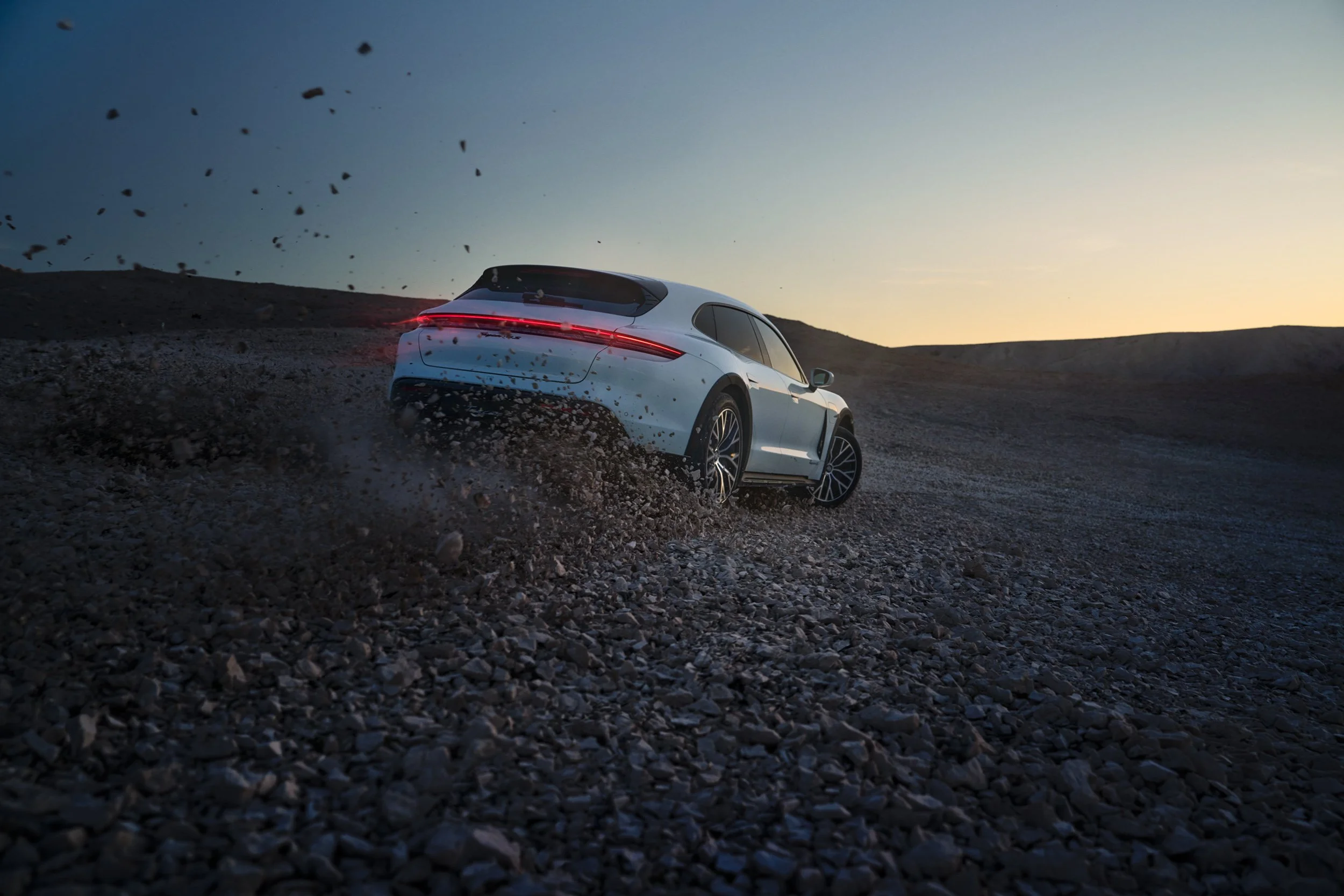 High-end automotive image of a white electric SUV drifting on rocky desert terrain at sunset, showcasing cinematic lighting and professional retouching.