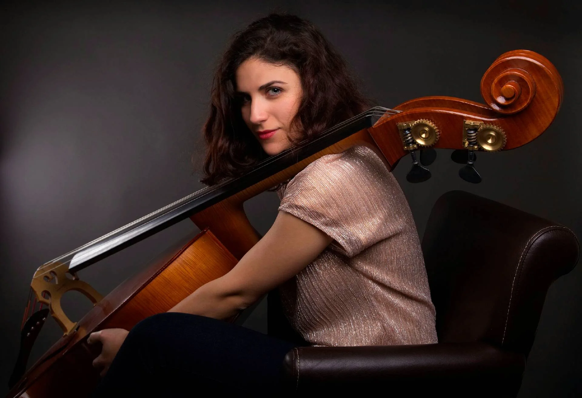 Woman seated holding a cello against a dark background.