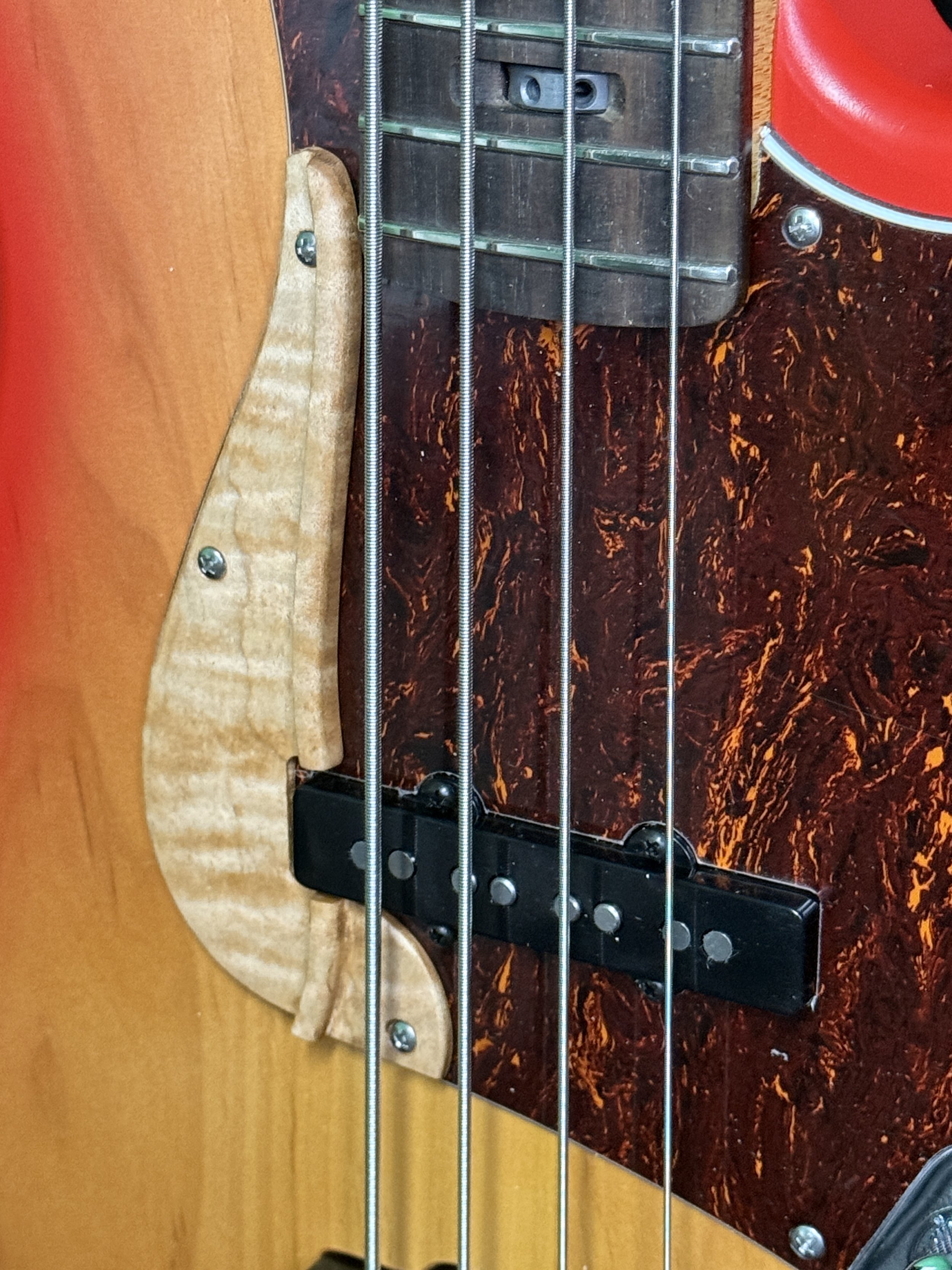 Close-up of a bass guitar's strings, wood pickguard, pickups, and body.