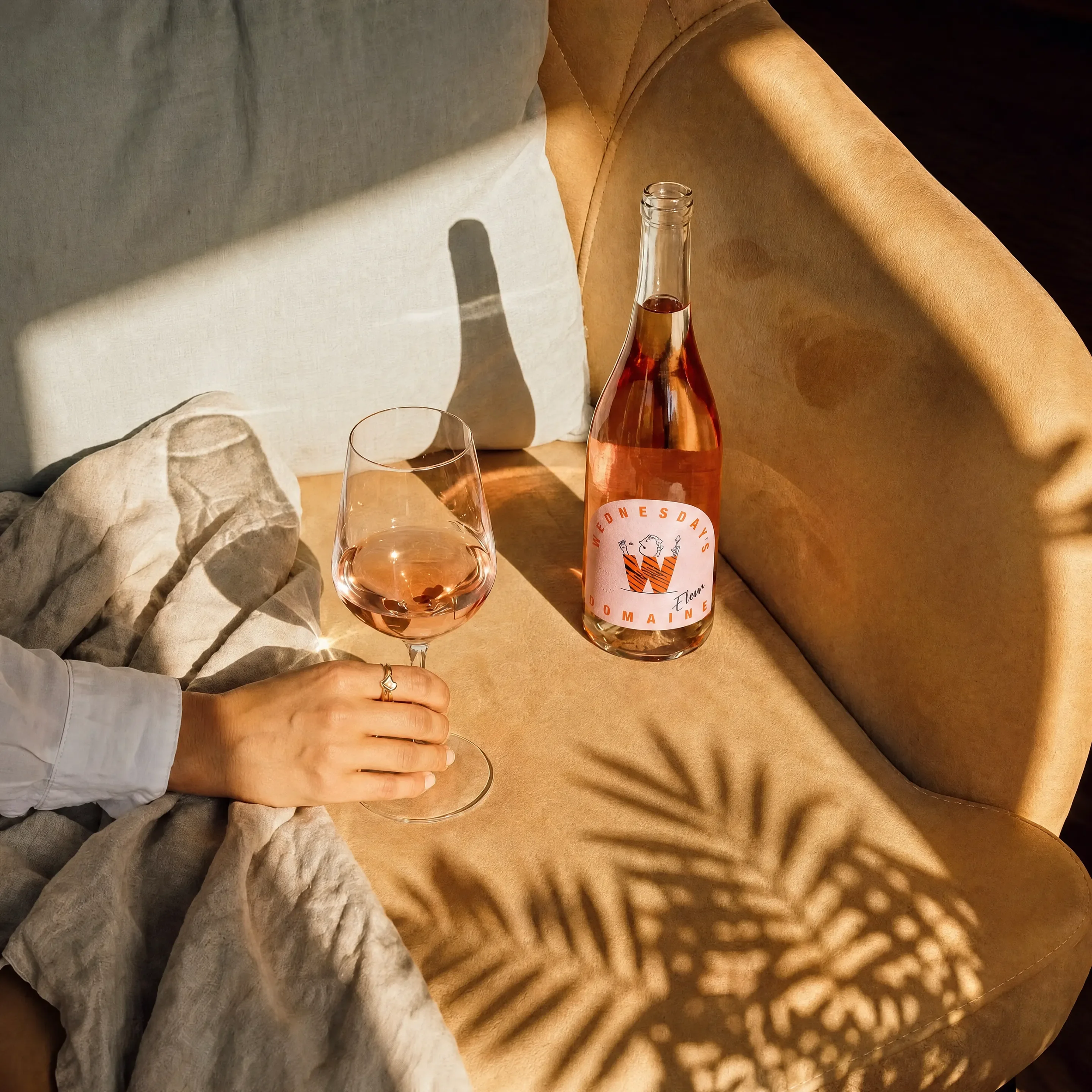 Wednesday domaine on a chair with a glass of rose. A woman is reaching out for the wine. Graphic Designer Creative Lead.