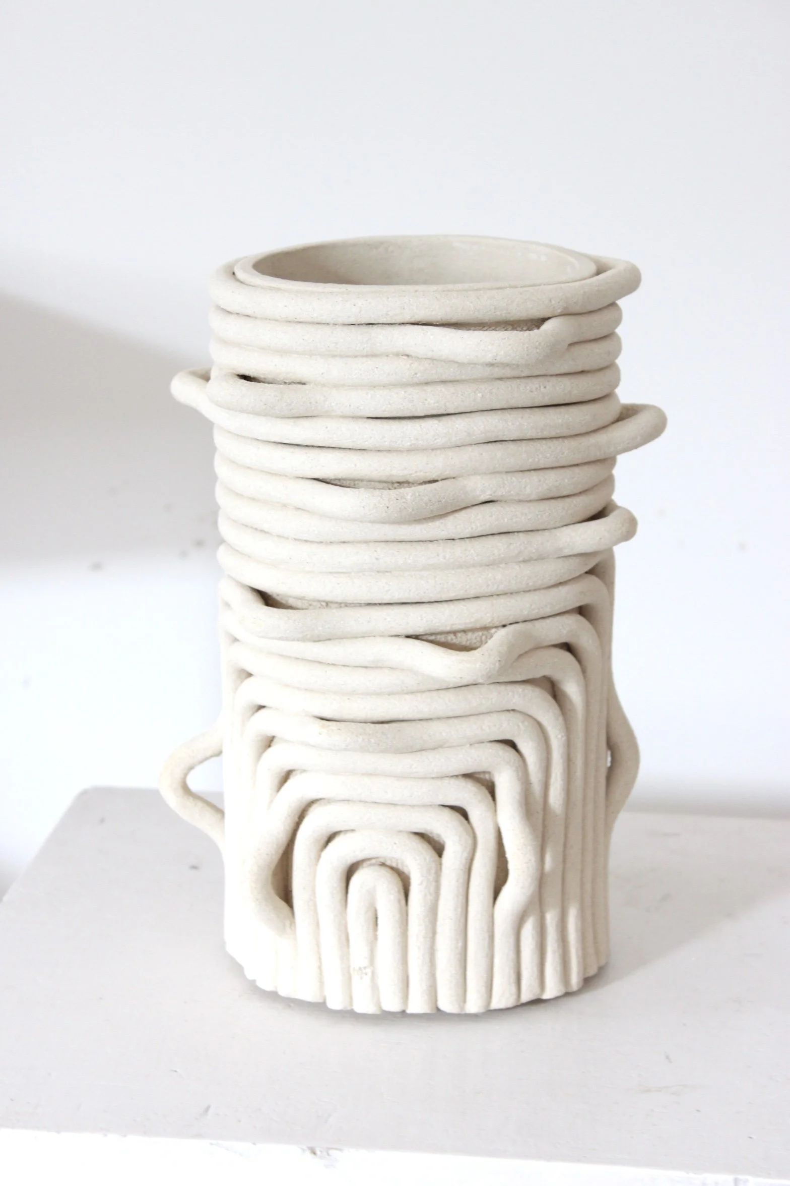 Vase en céramique blanc aux formes organiques empilées avec des courbes et des motifs en boucle.