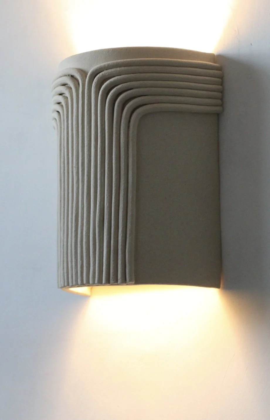 Applique murale moderne avec design en bandes courbées en matériau beige, éclairant la wall.