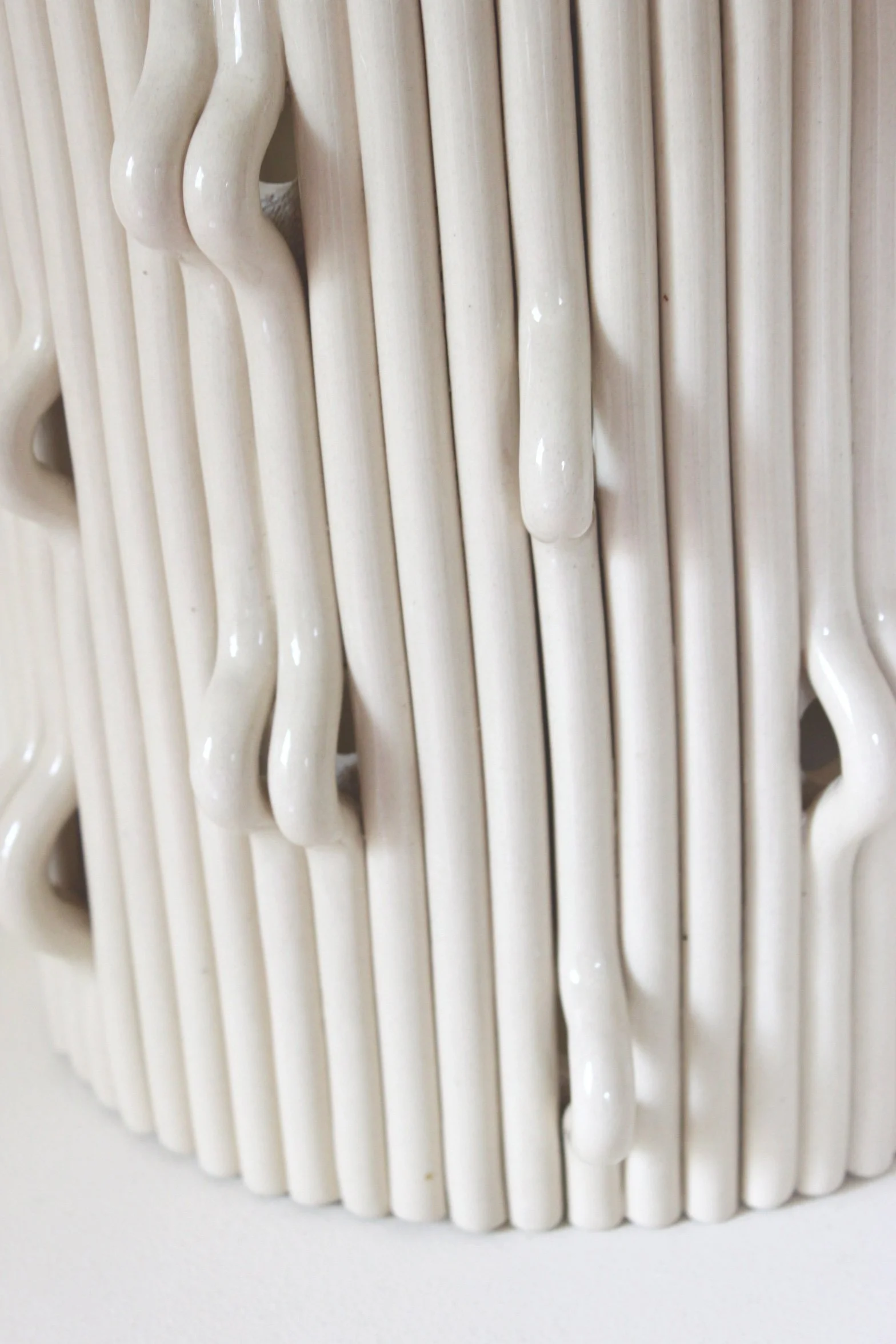 Une sculpture moderne blanche composée de bâtons de céramique ou de plastique, avec certains qui semblent avoir de la glaçure ou de la pâte qui coule, en forme de cercle ou de spirale.