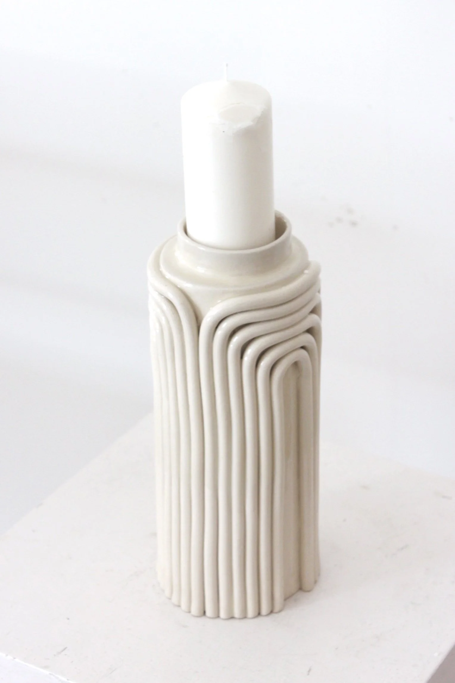 Une bougie blanche dans un support en céramique blanc avec un design en lignes courbes.