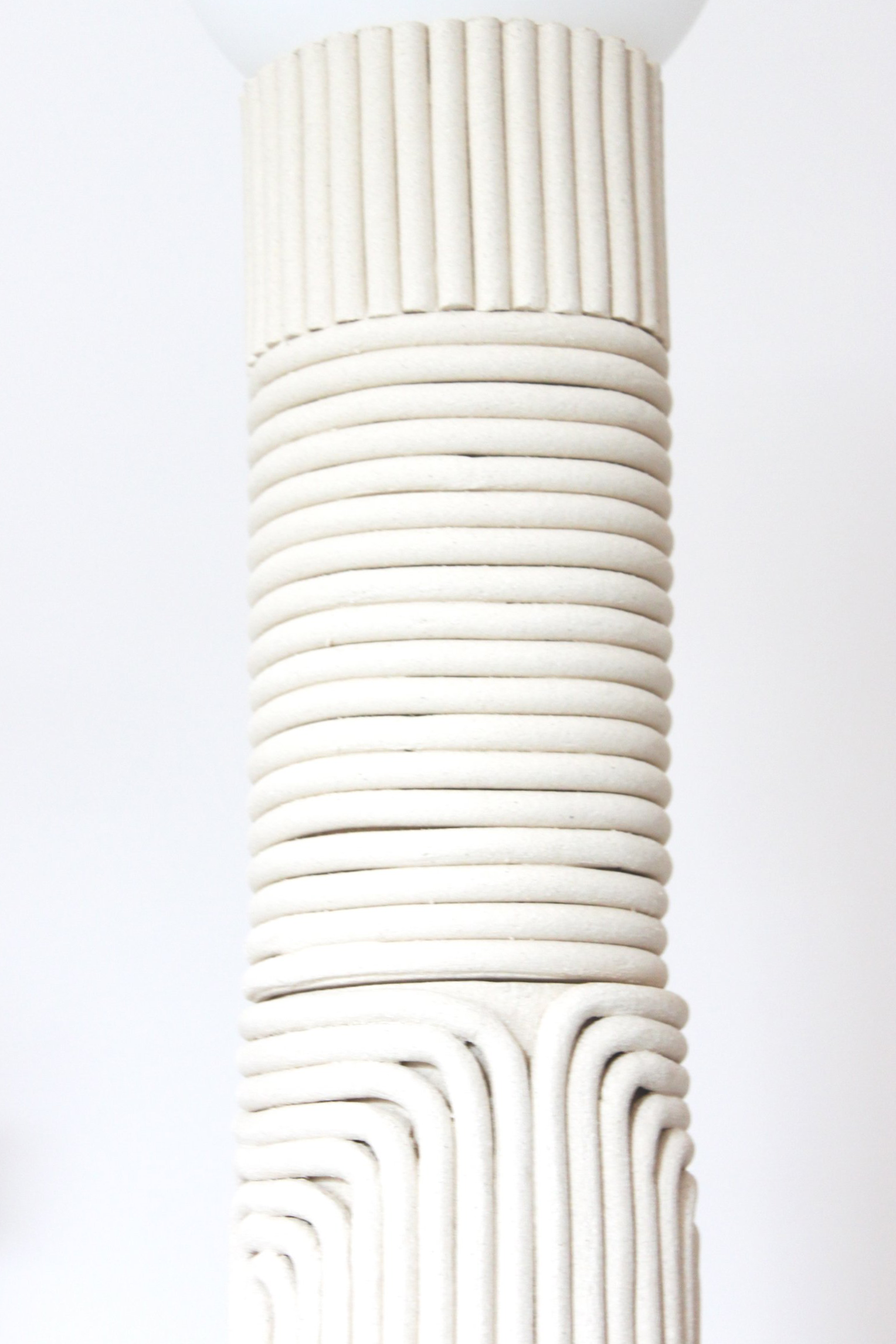 Une sculpture moderne en relief blanc avec des motifs géométriques répétés et des formes ondulantes.