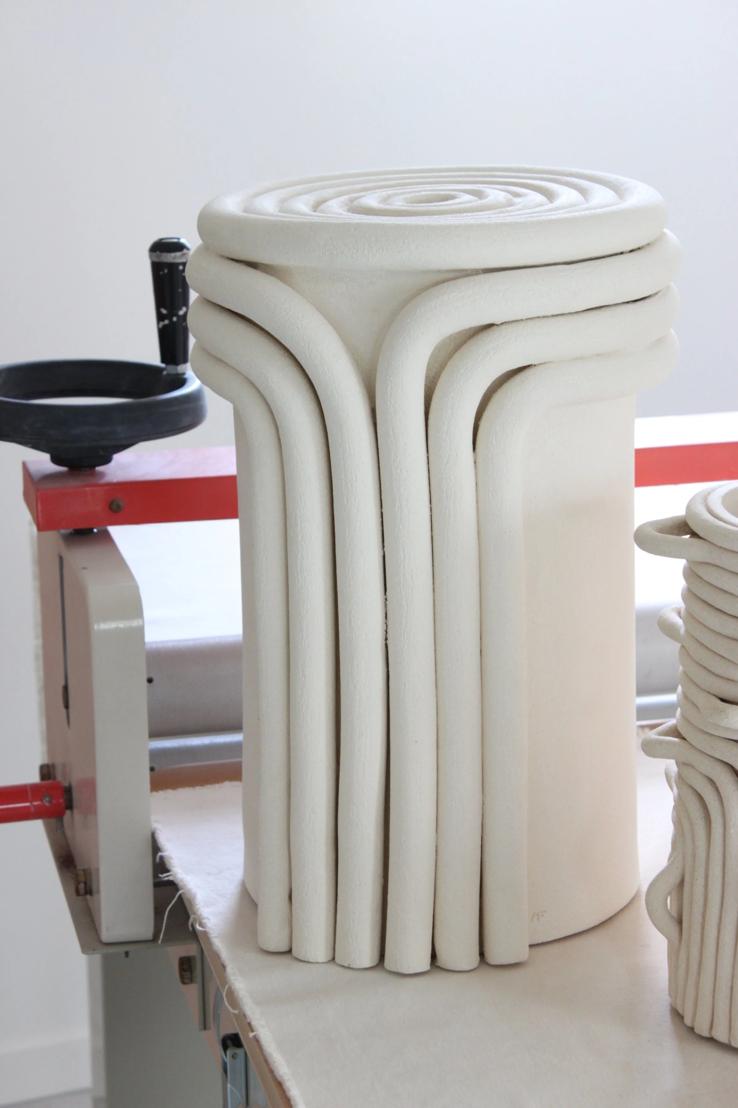 Sculpture blanche en forme de tour avec des spirales en haut, sur une table, près d'un petit atelier de sculpture.