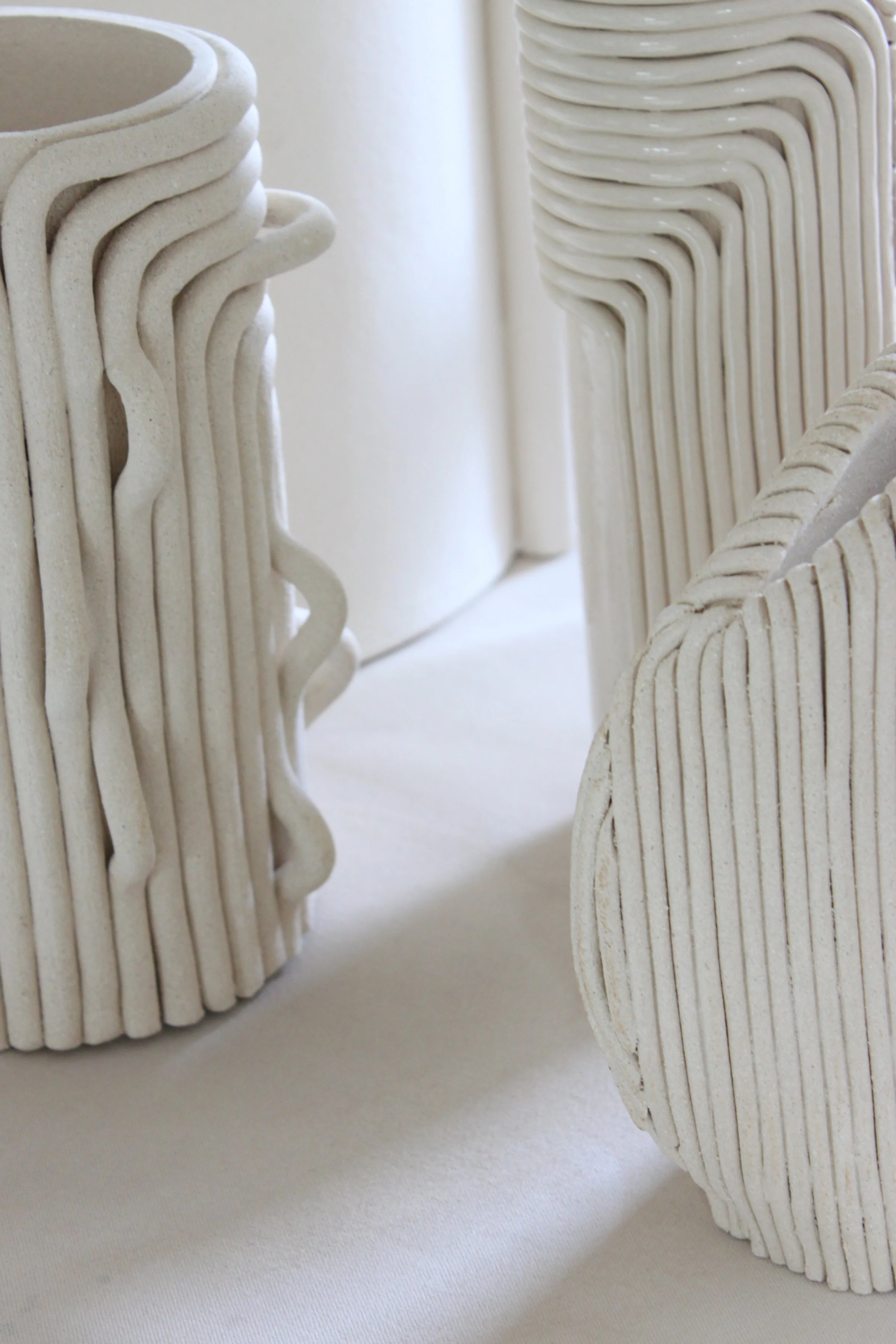 Objets décoratifs en forme de livres faits de matériaux légers, blancs ou beige, empilés verticalement sur une surface blanche.