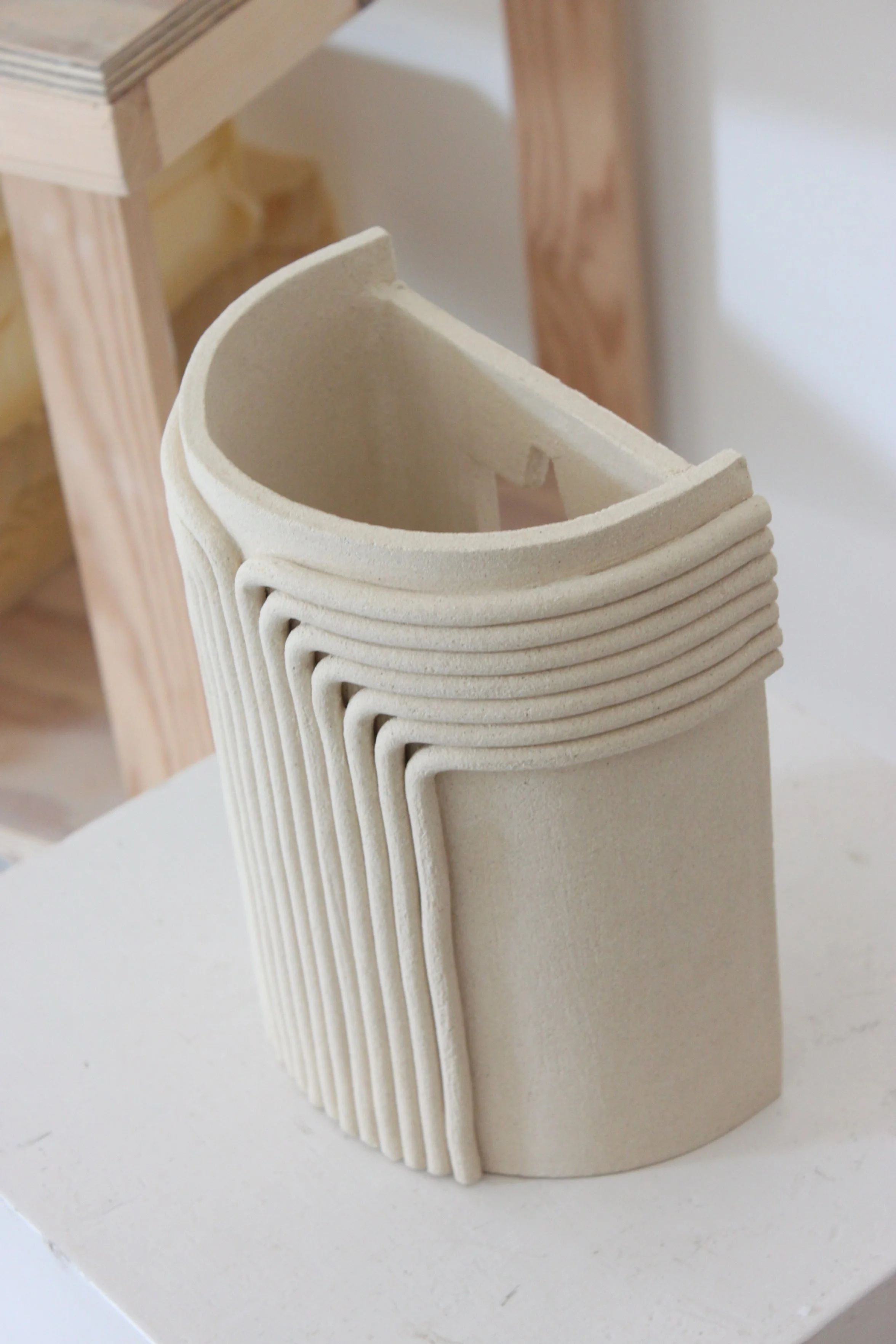 Maquette en argile de formes architecturales avec courbes et lignes, placée sur une surface blanche.