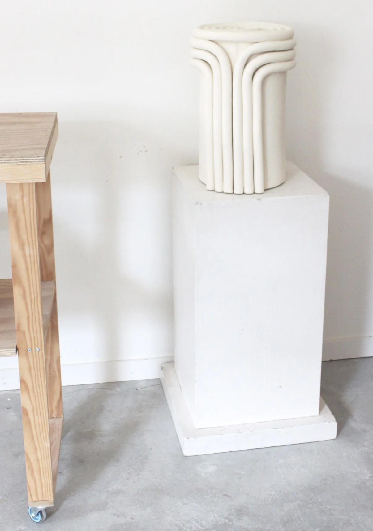Une sculpture en céramique ou en marbre de forme cylindrique avec des lignes incurvées et des motifs en boucle, placée sur un socle blanc en plâtre ou en béton.
