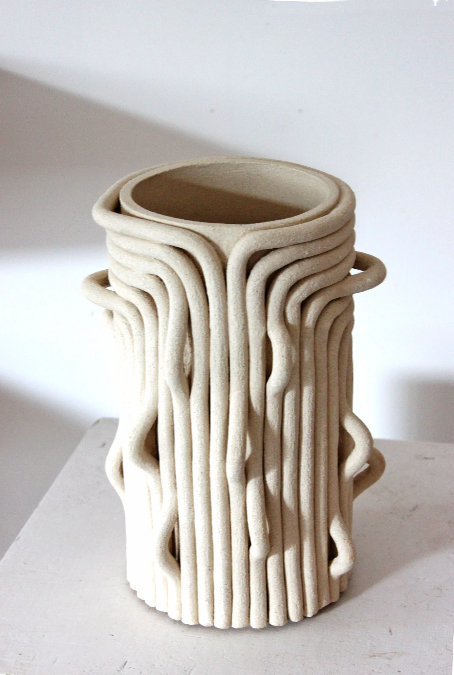 Vase en céramique beige avec un design de lignes ondulées, posé sur une surface blanche.