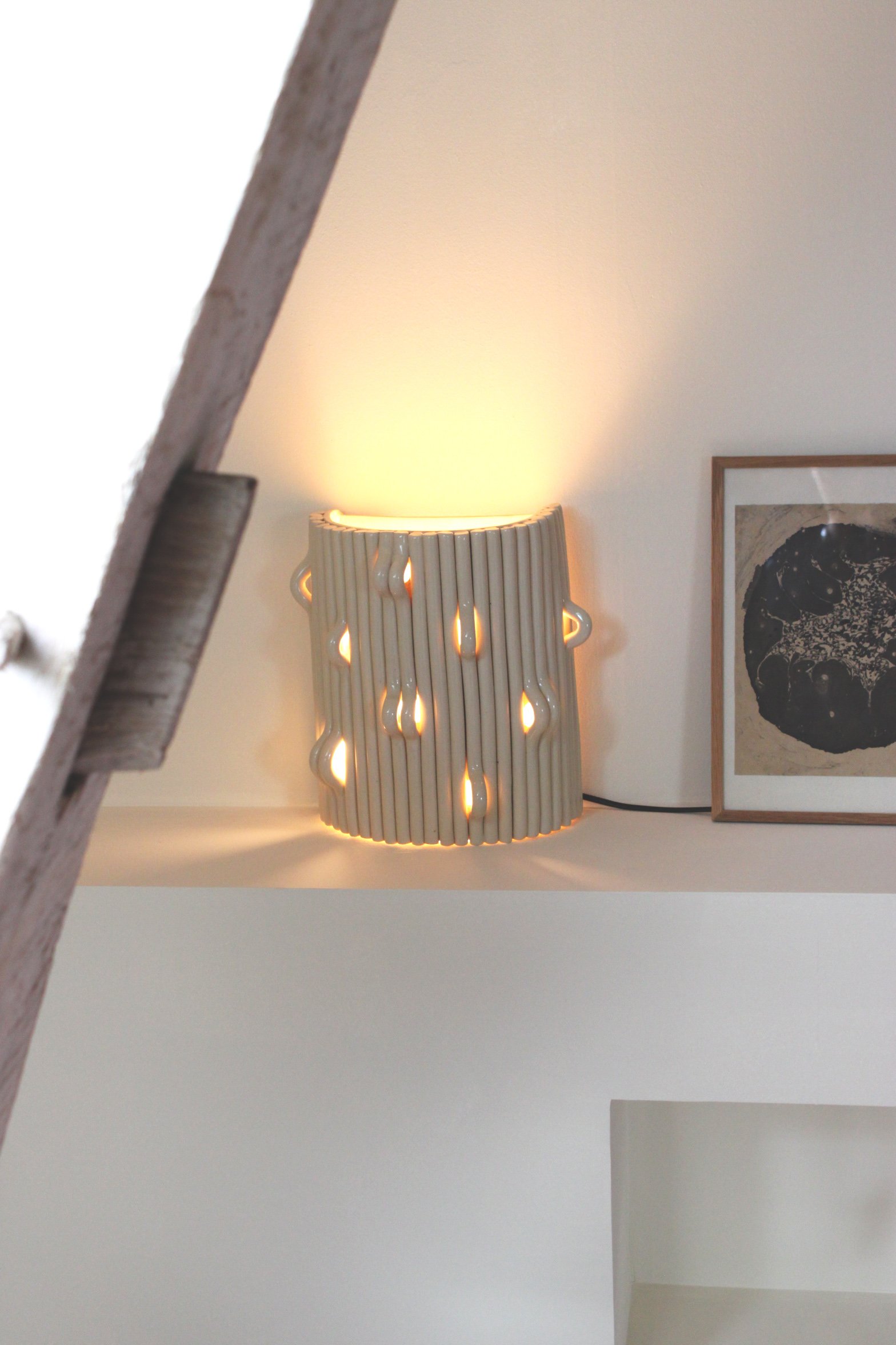 Lampe décorative en céramique avec motifs de gouttes d'eau, éclairée, placée sur une étagère à côté d'un tableau abstract.