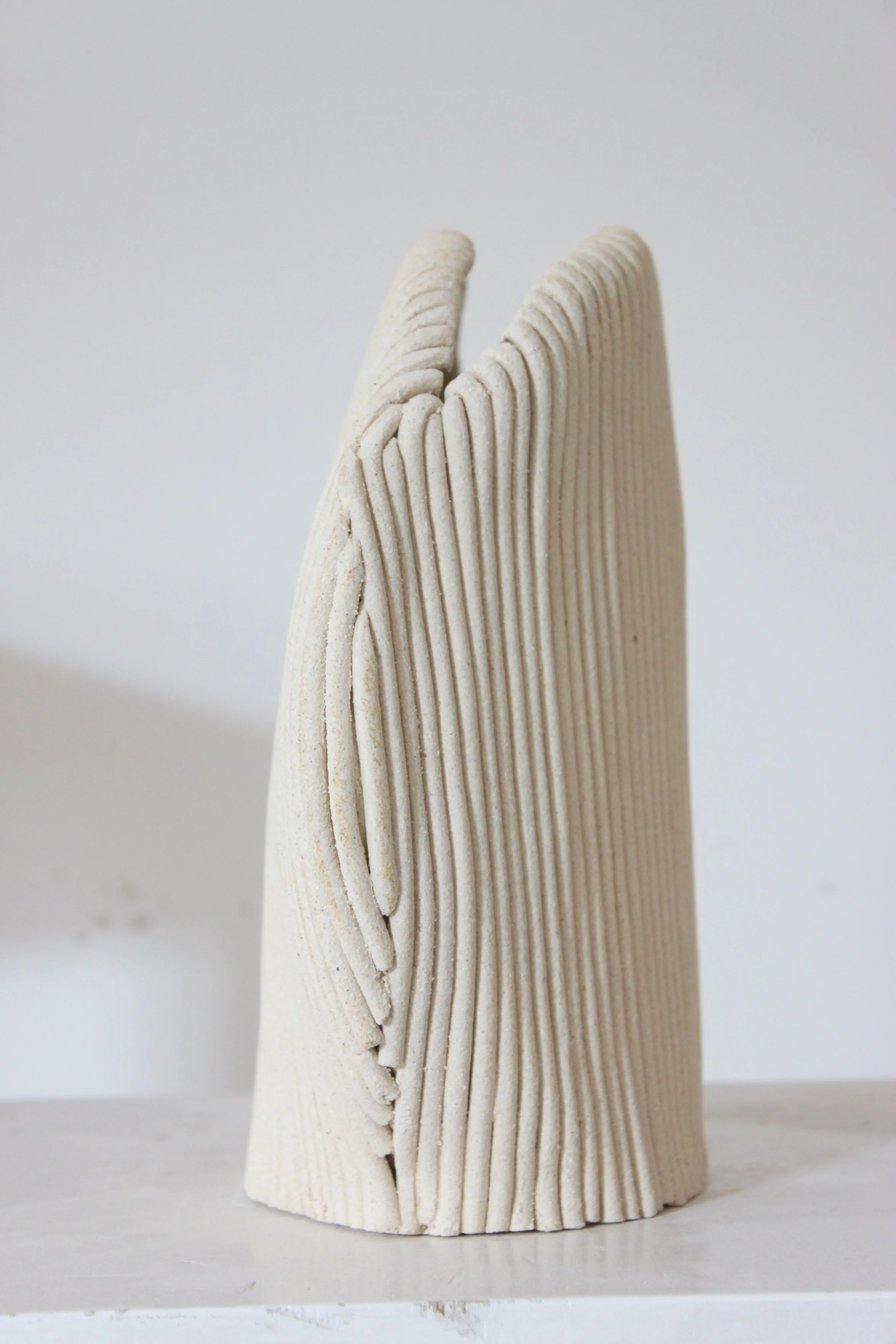 Sculpture en céramique beige avec une texture torsadée et des lignes verticales, placée sur une surface blanche