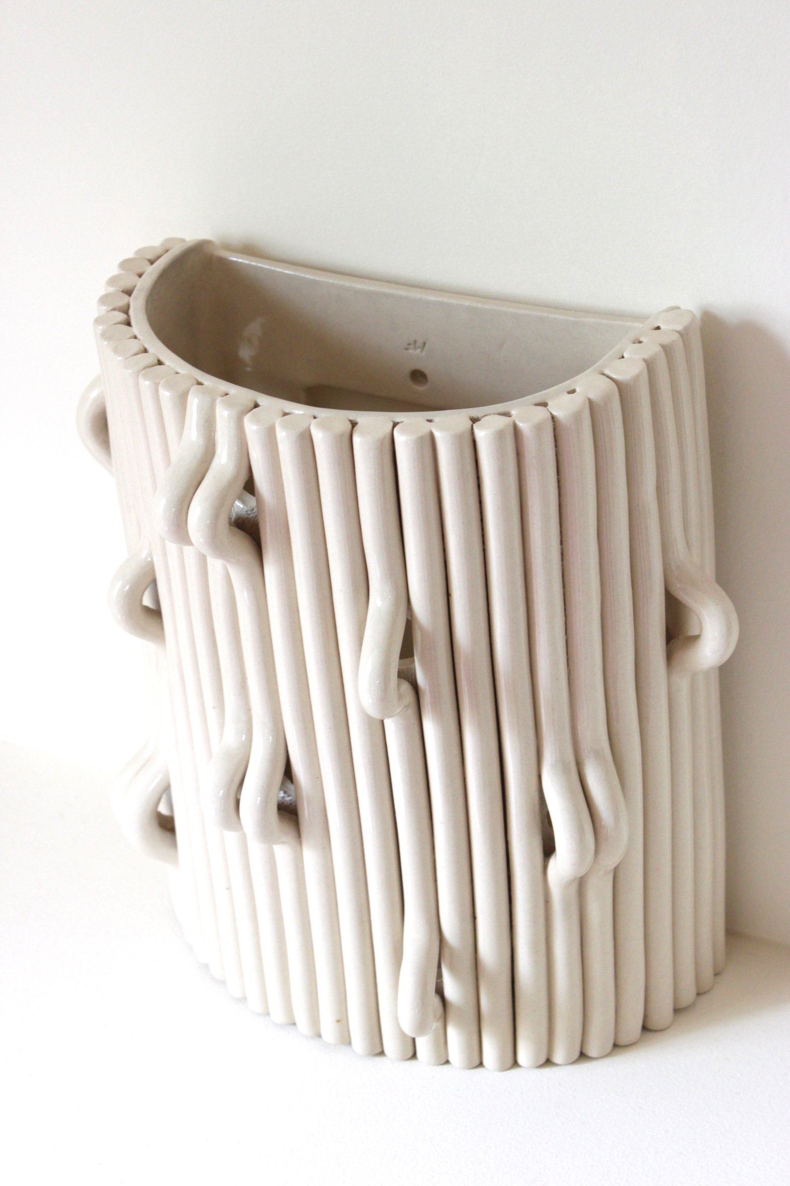 Vase en céramique blanc avec un design artistique de tubes cylindriques et de mèches qui pendent le long de ses côtés.